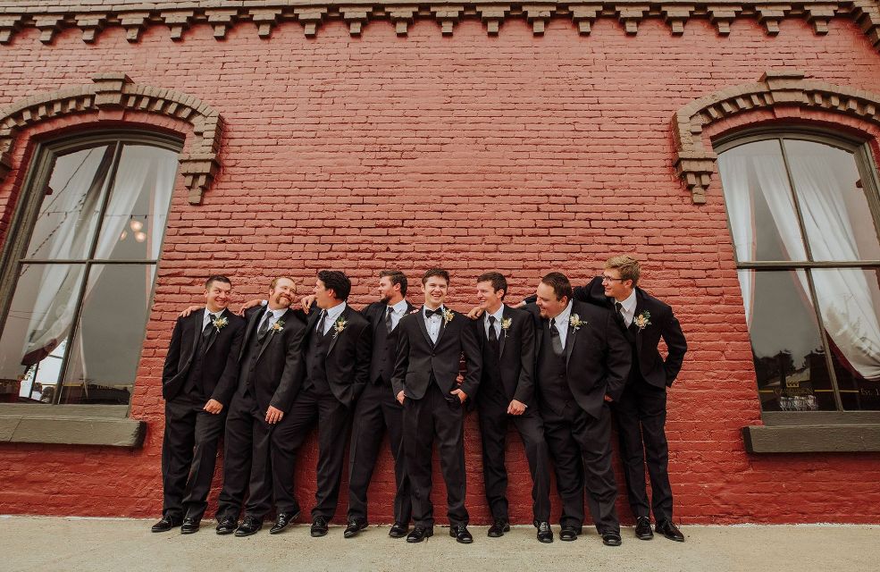 The groom and his groomsmen are posing for a picture in front of a red brick building.