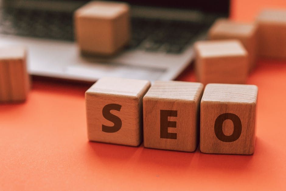 Wooden blocks spelling SEO on an orange surface with a blurred laptop in the background