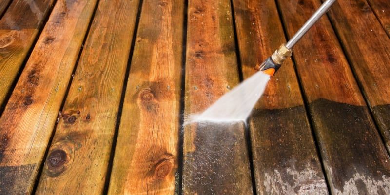 a person is cleaning a wooden deck with a high pressure washer .