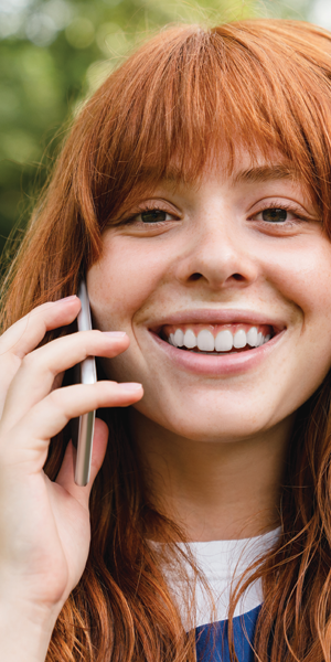 Woman with red hair smiling while talking on a cell phone.