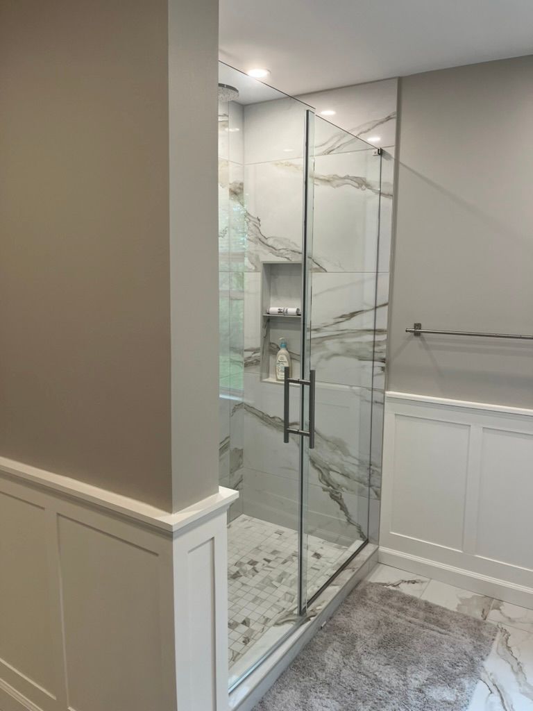 Modern bathroom with glass shower enclosure, marble-look tile, and recessed shelf. Grey and white tones.