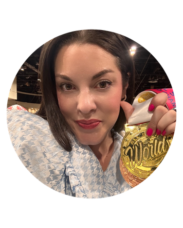 Woman holding a gold medal, pink lipstick, floral blouse.