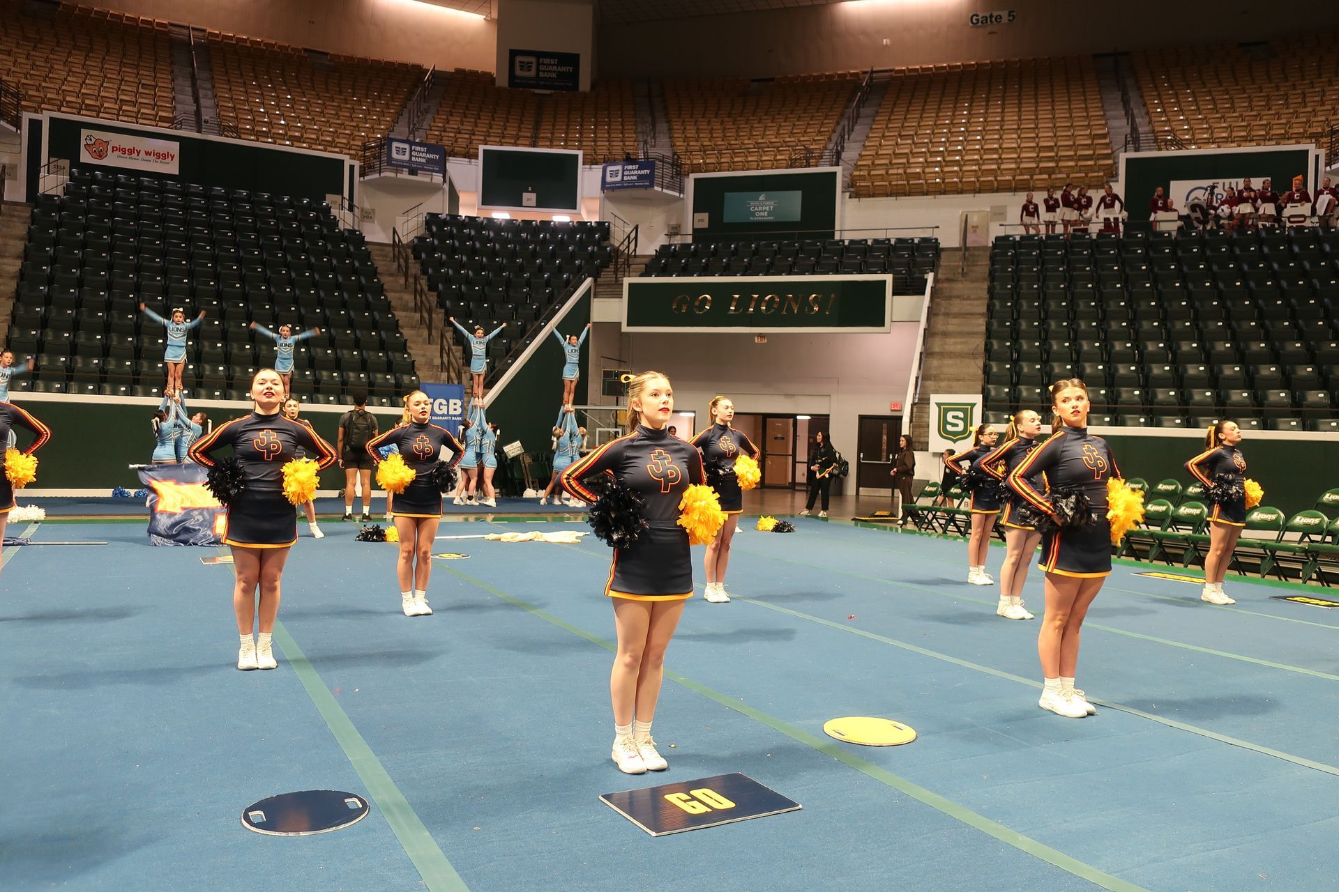 Cheerleaders in blue and gold uniforms performing in an arena, some with pom-poms, others in a stunt.
