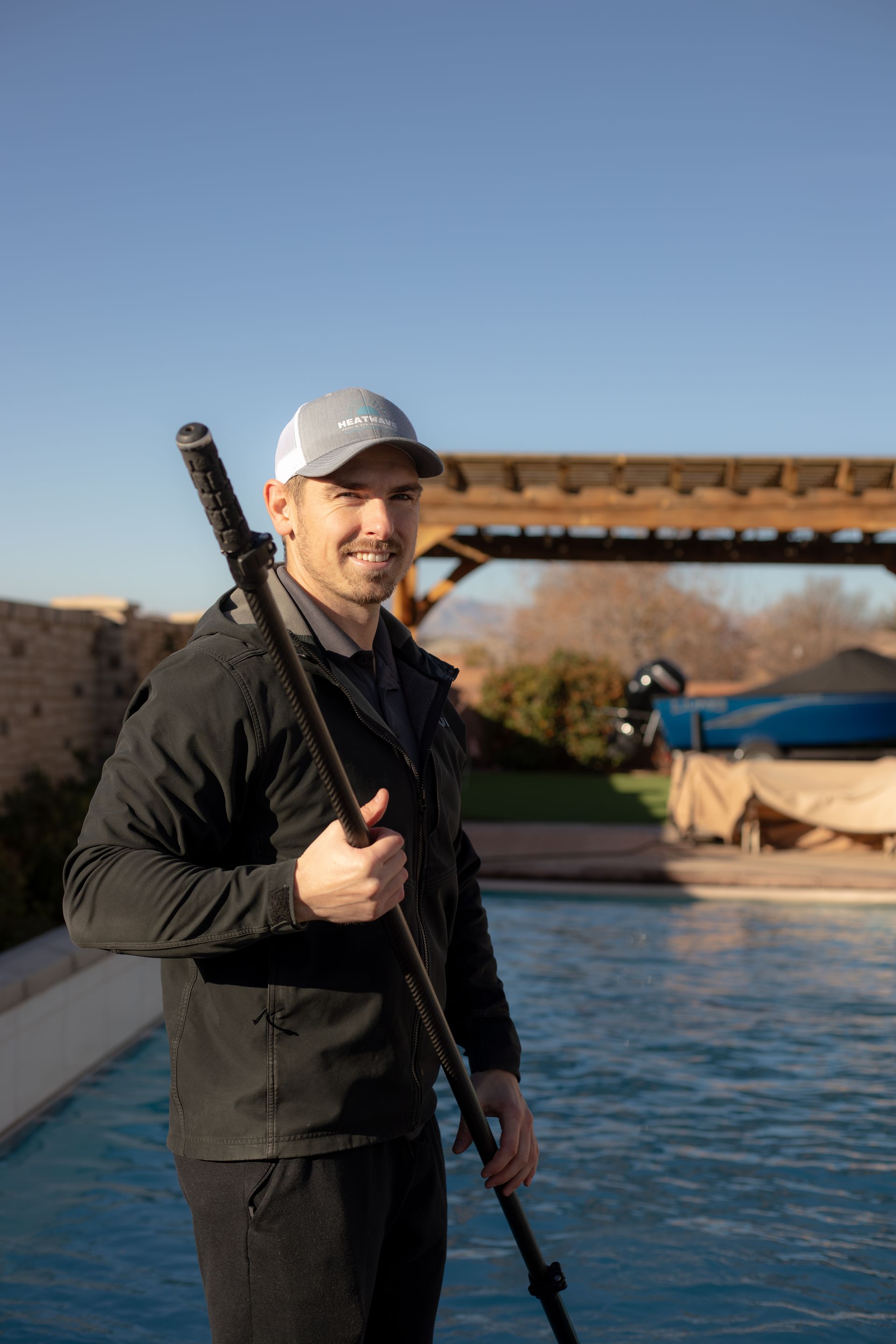 pool boy smiling at the camera while holding a pool pole standing next to a backyard pool in Southern Utah.