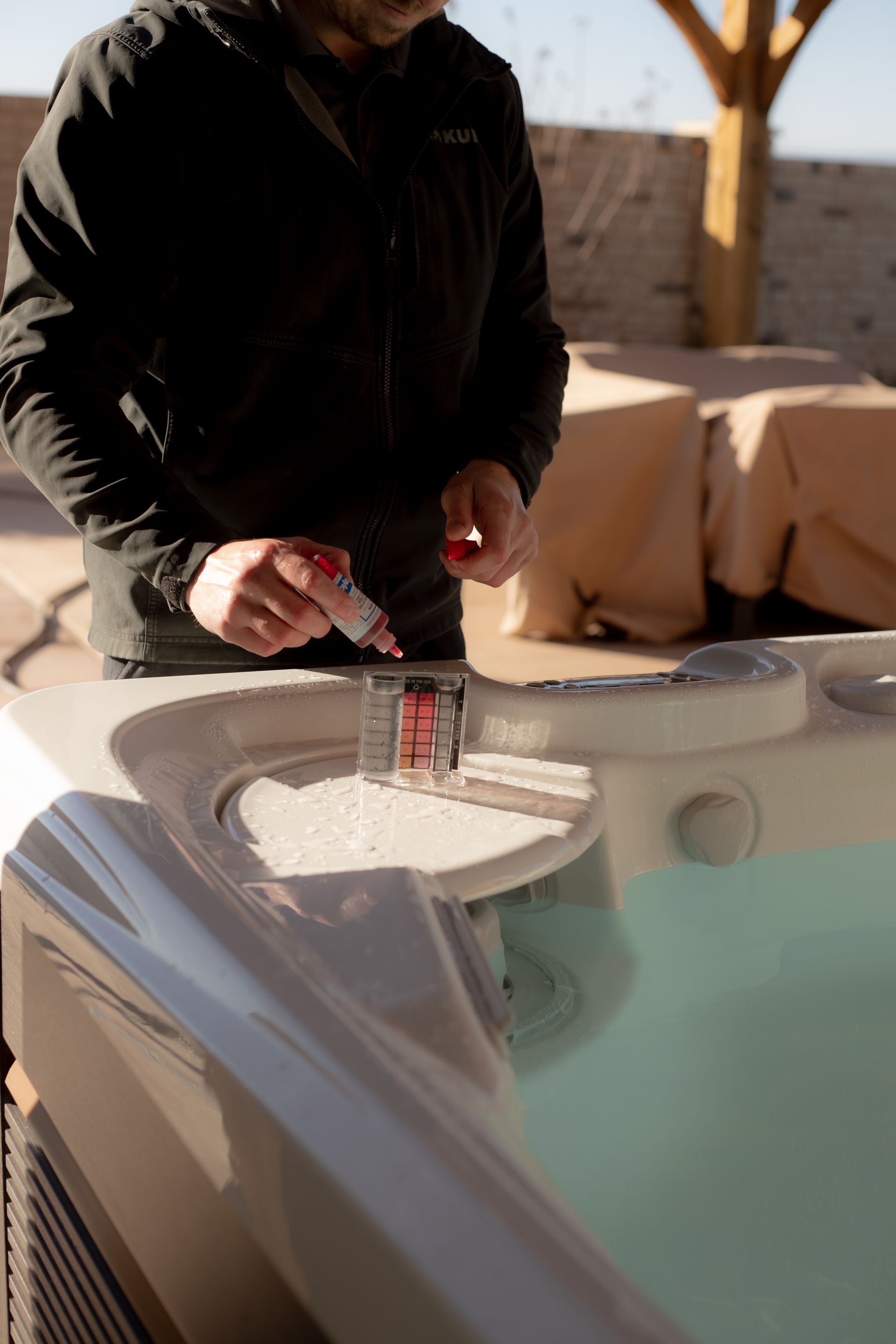 Weekly hot tub maintenance being preformed at the edge of the hot tub testing the chemicals in a St. George backyard. 