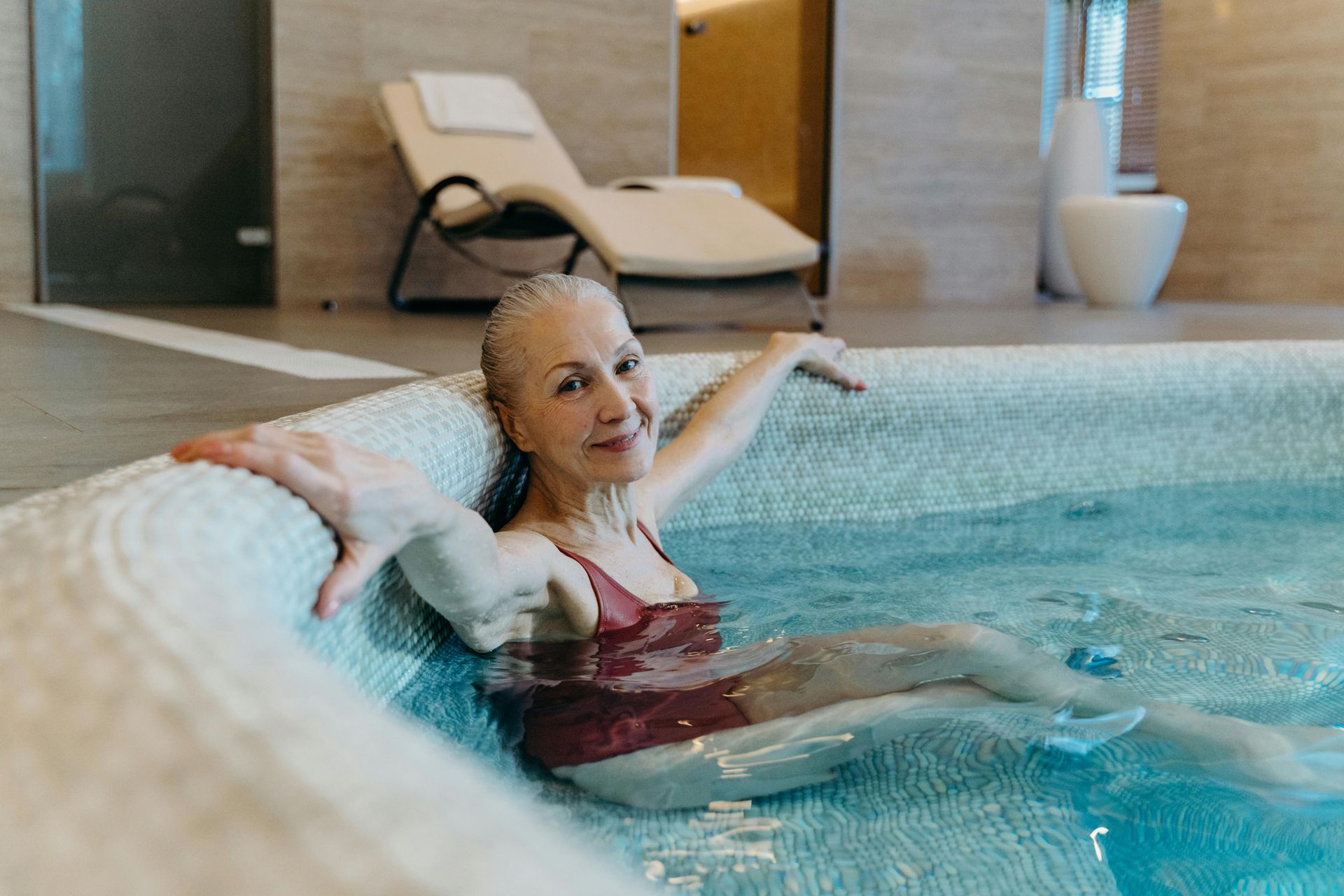 Women sitting in a well maintained hot tub smiling at the camera with a lounge chair behind her. 