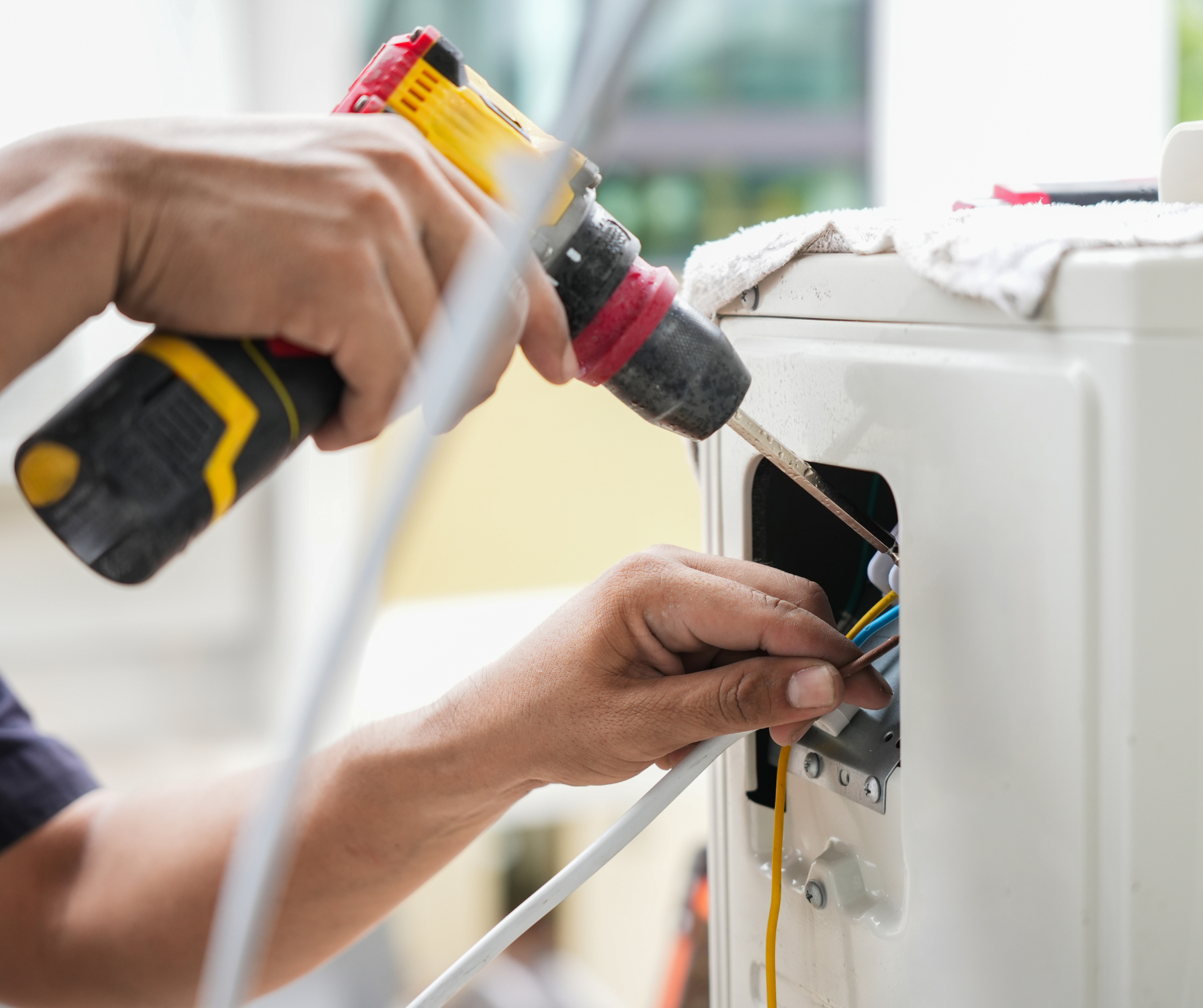 Person using a drill to install wires into an electrical box on a white appliance.