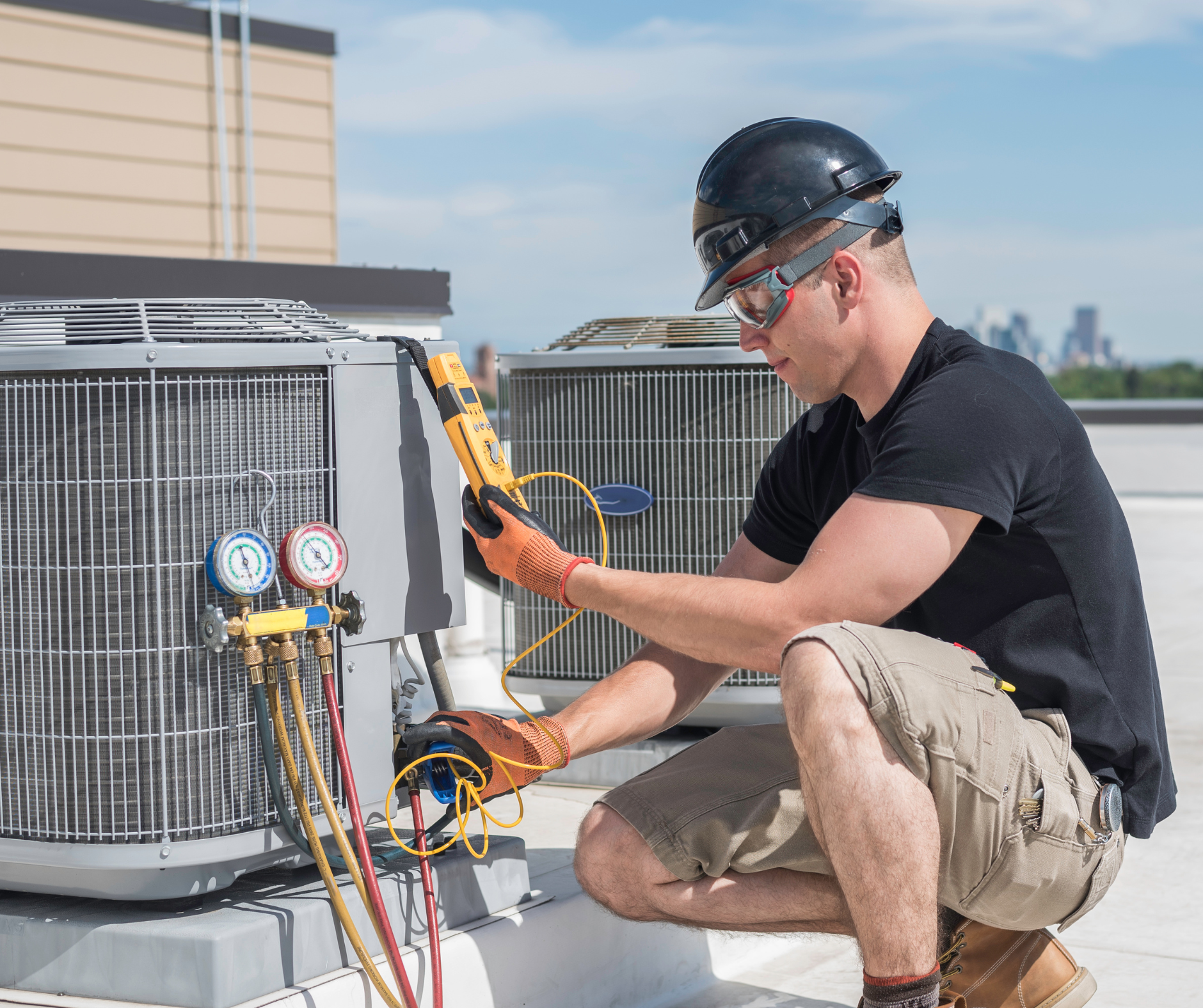 HVAC technician checks rooftop air conditioner with a meter, wearing safety glasses and a hard hat.
