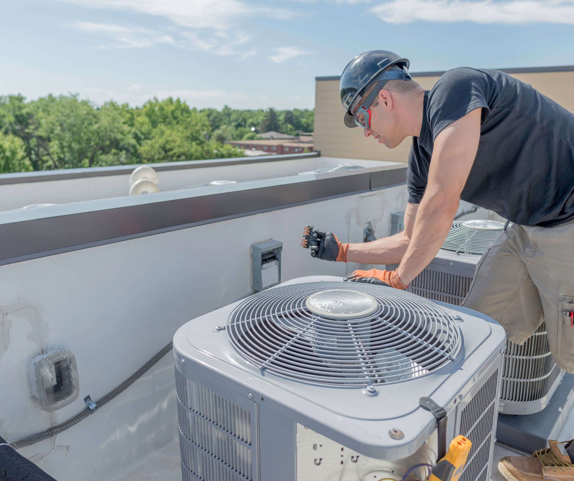 HVAC technician working on an air conditioning unit on a rooftop on a sunny day.