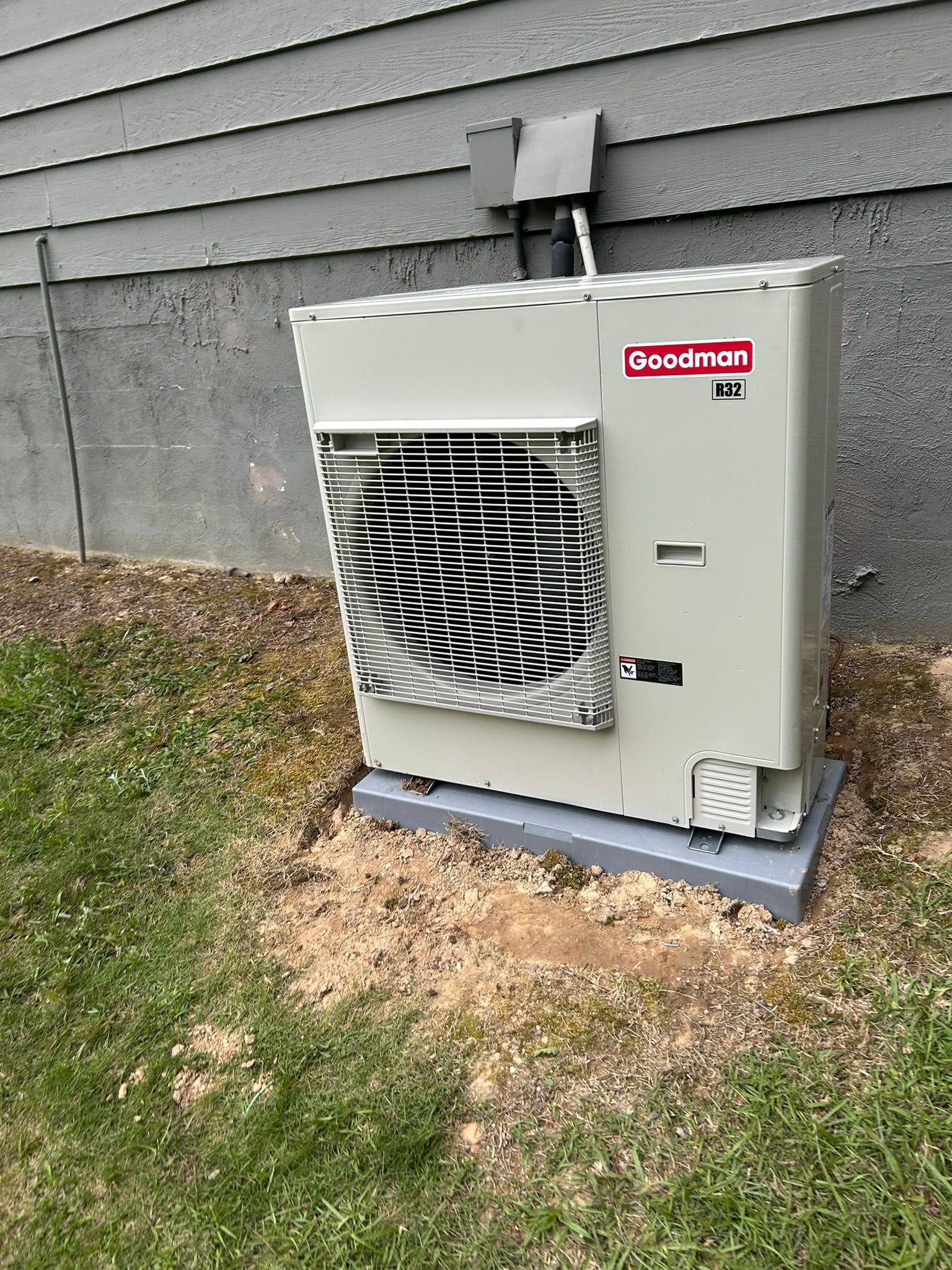 Goodman brand air conditioning unit outside a building, set on a concrete pad.
