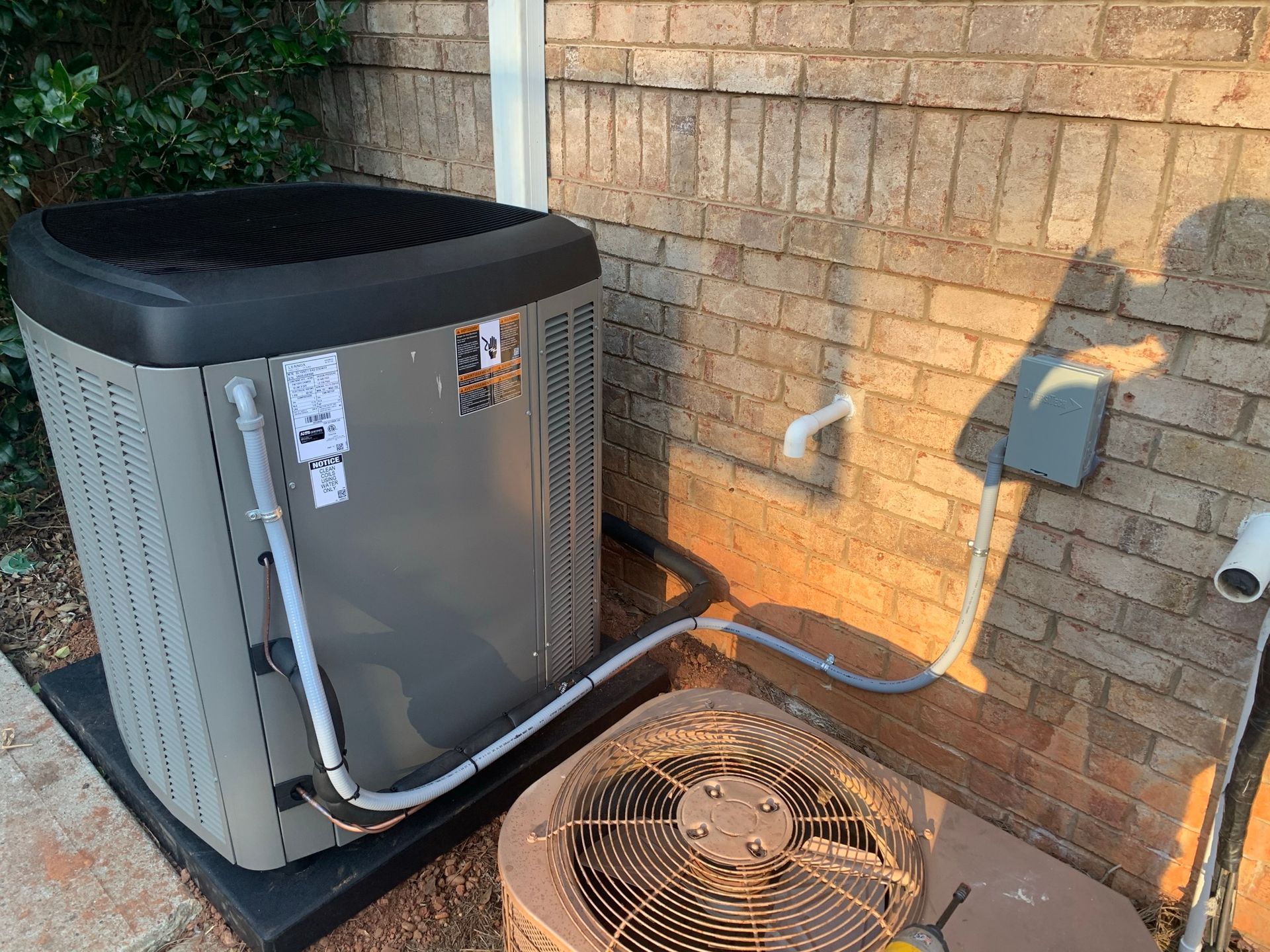 A technician working on an AC unit, connecting hoses to a gauge, next to a refrigerant tank.