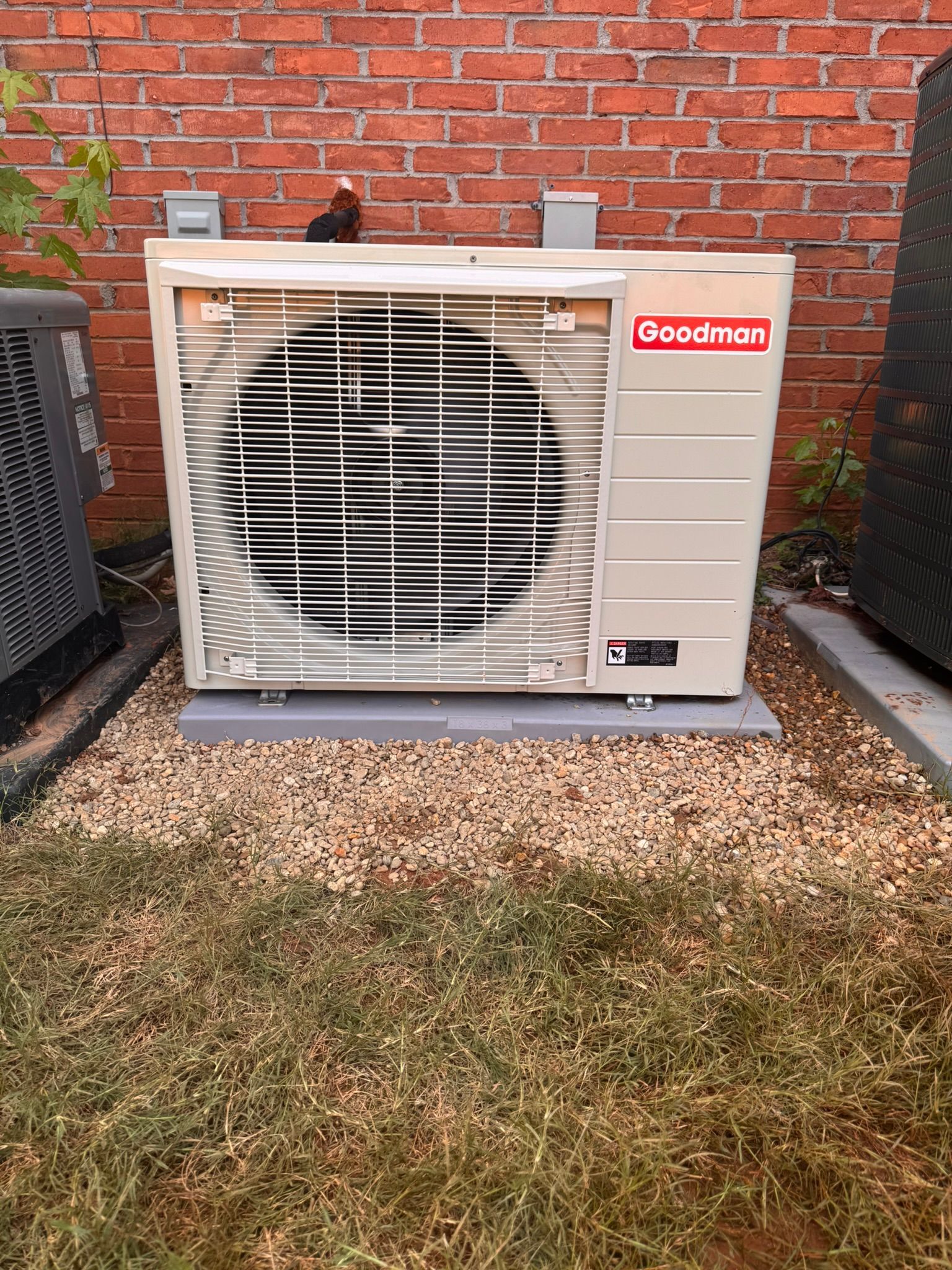 Goodman air conditioner unit on a gravel bed next to a brick wall.