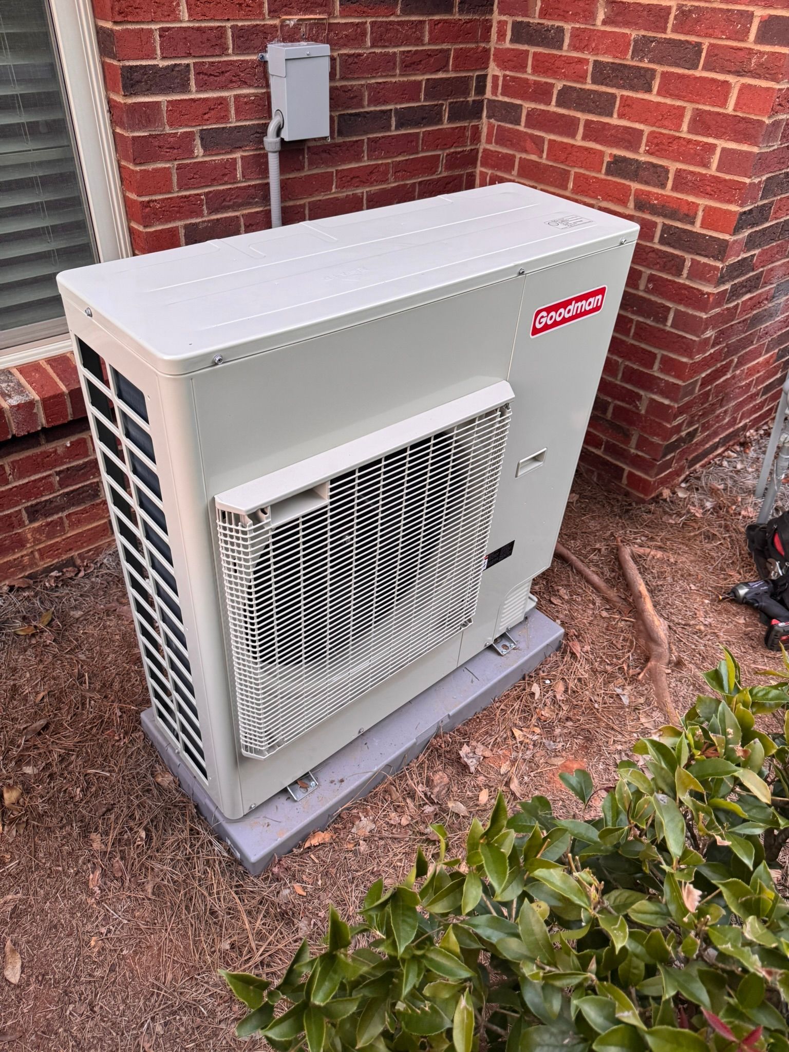 A white outdoor heat pump unit next to a brick wall.