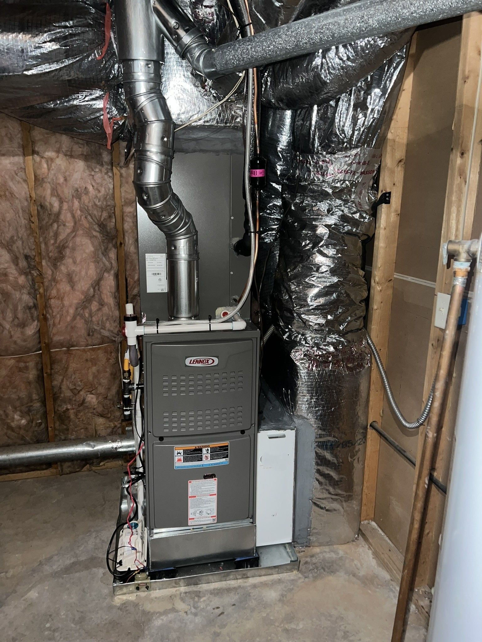 Furnace unit in a basement. Ductwork and insulation visible. Grey and silver tones.