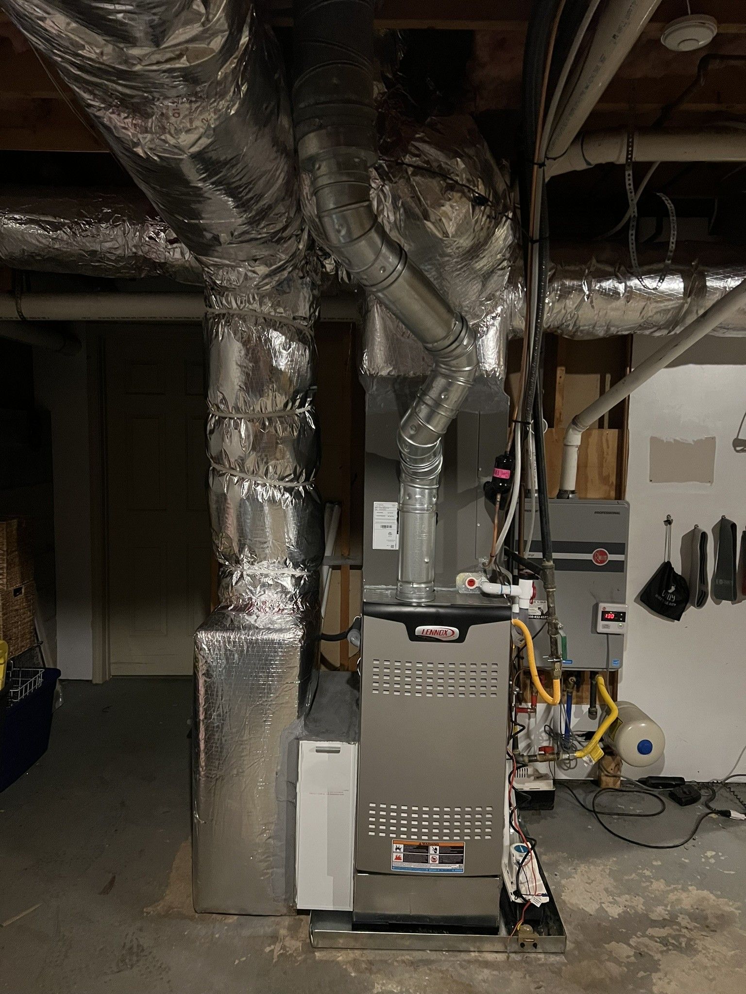 HVAC system in a basement. Silver ductwork, furnace, and a water softener on a concrete floor.