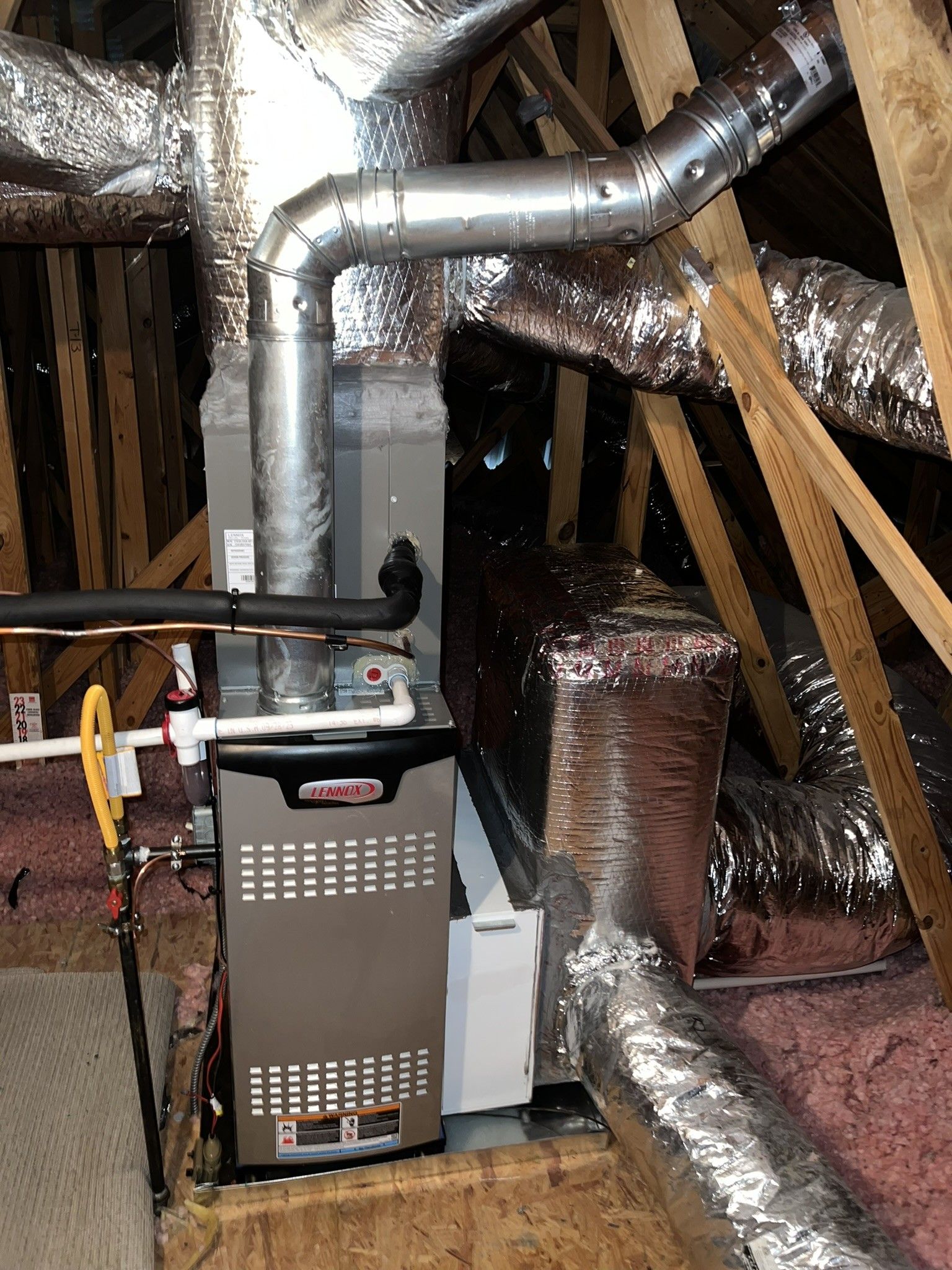 HVAC system in attic: furnace with metal ductwork and insulation, wooden rafters, and gas line.