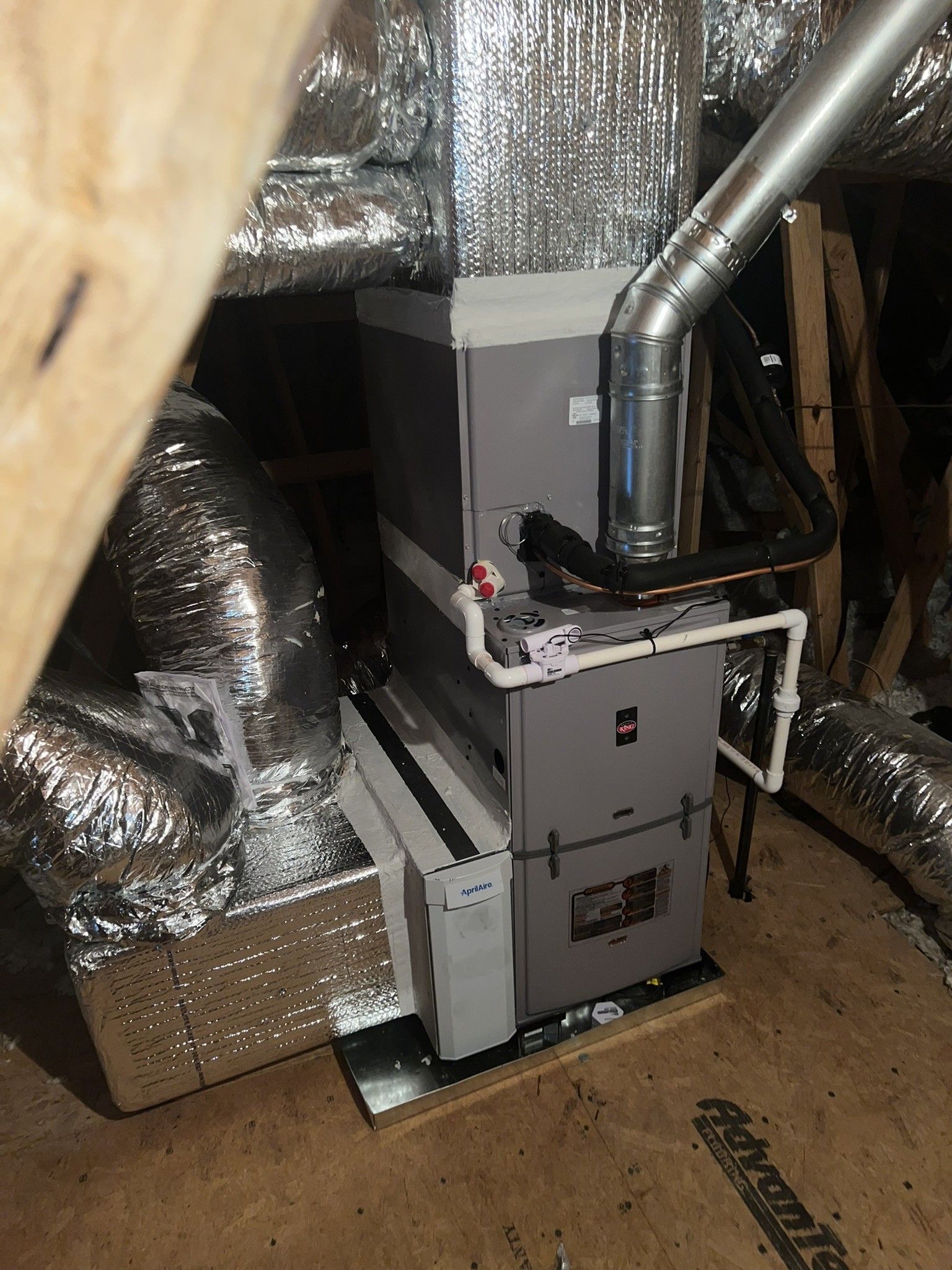HVAC system in an attic. Ductwork, gas pipe, and flue are attached to the gray unit.
