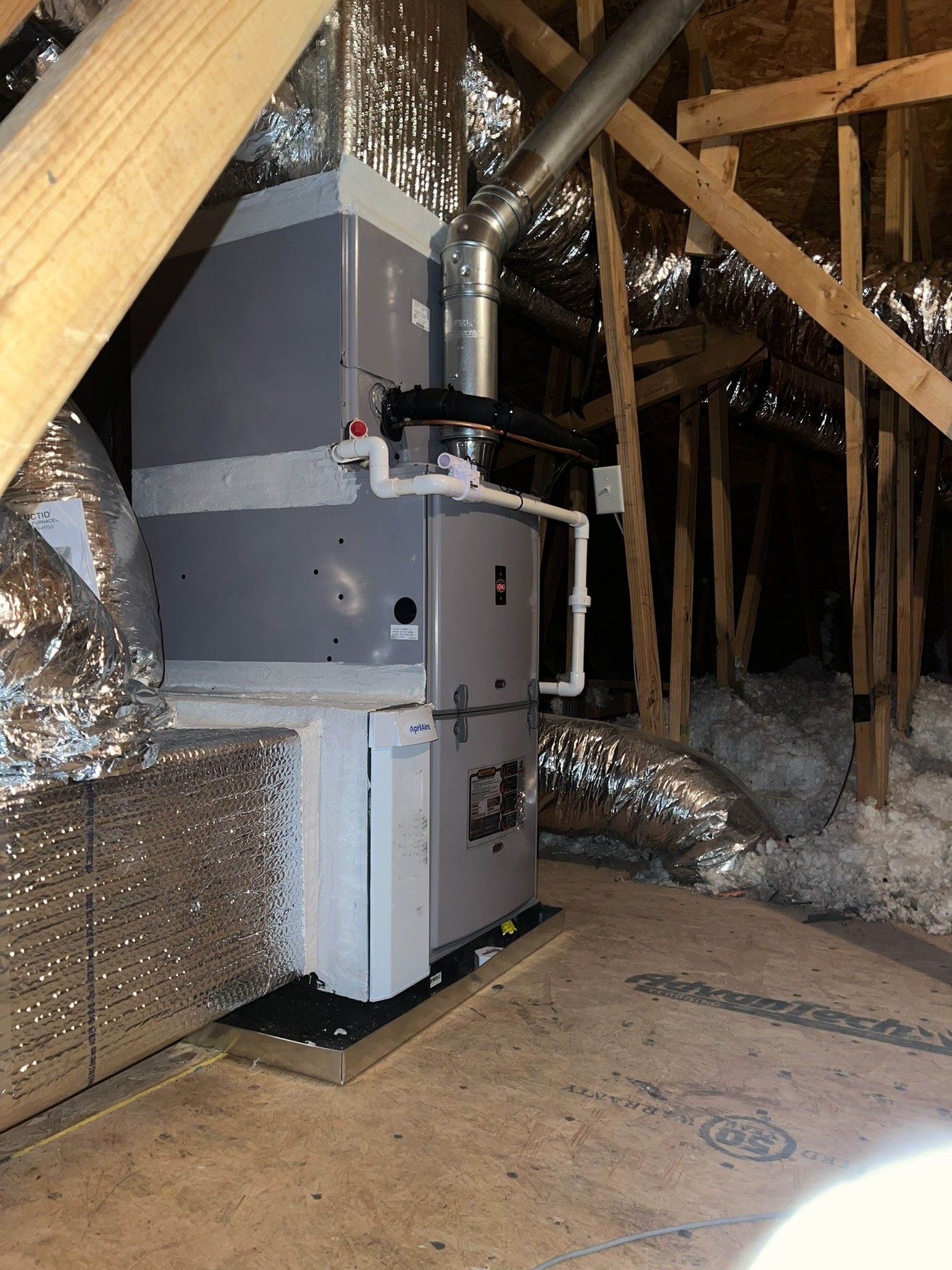 HVAC system installed in an attic with ductwork, gray and silver, on a wooden platform.