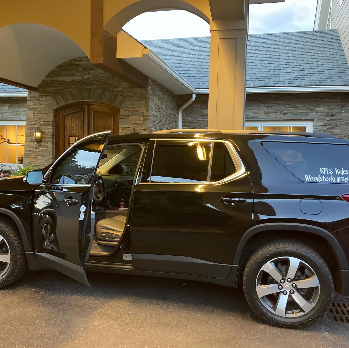 A black suv is parked in front of a house with the door open