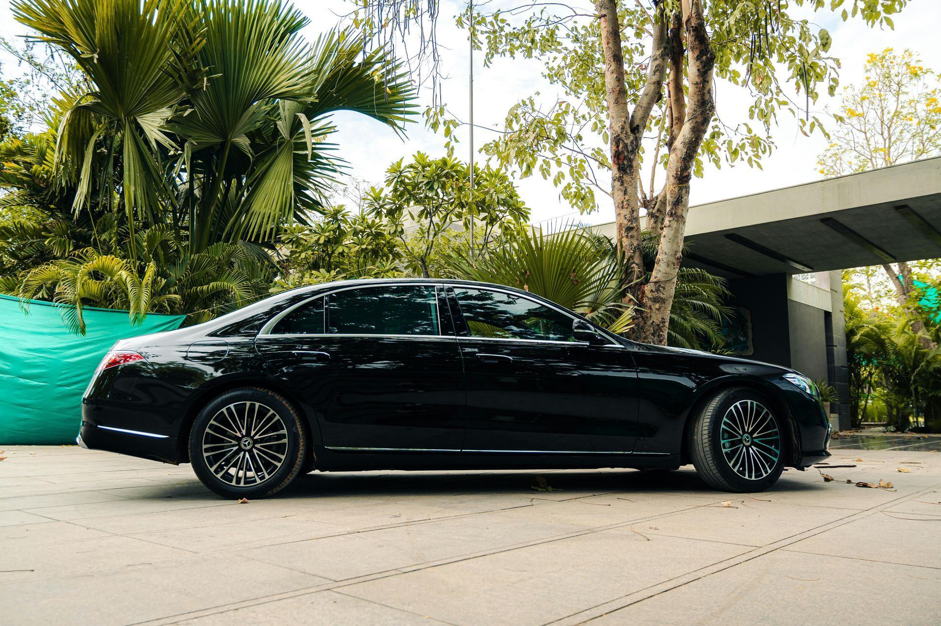 Black sedan parked outdoors beside palm trees and a modern building