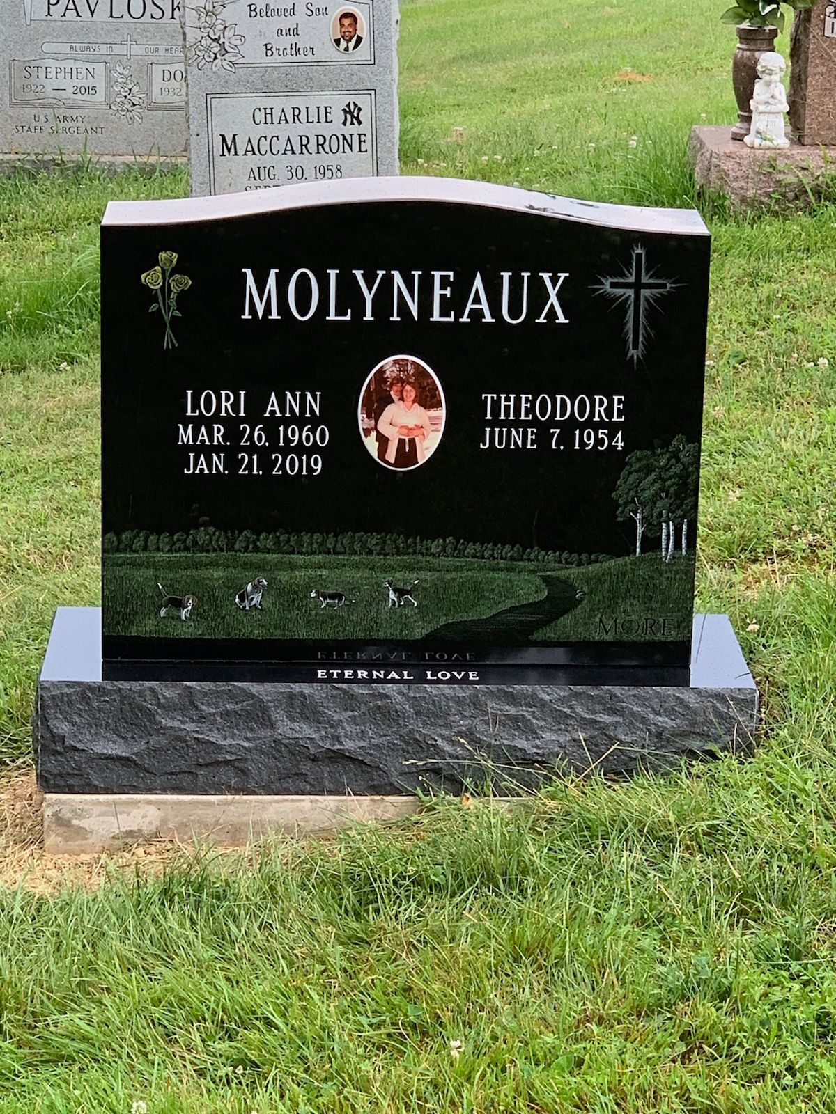 A black gravestone with a cross on it is in a cemetery.