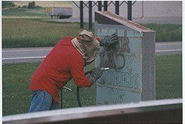 A man in a red shirt is sandblasting a sign.