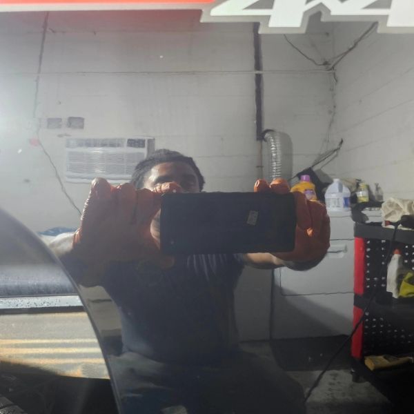 A person holding a phone to take a selfie reflection in the glossy side of a vehicle in a garage.