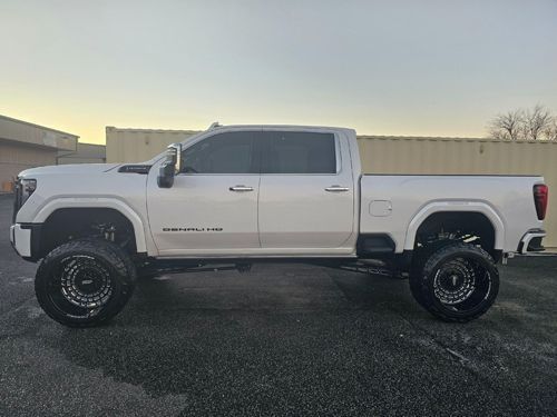 A white lifted GMC Denali pickup truck parked against a light-colored wall during the golden hour.