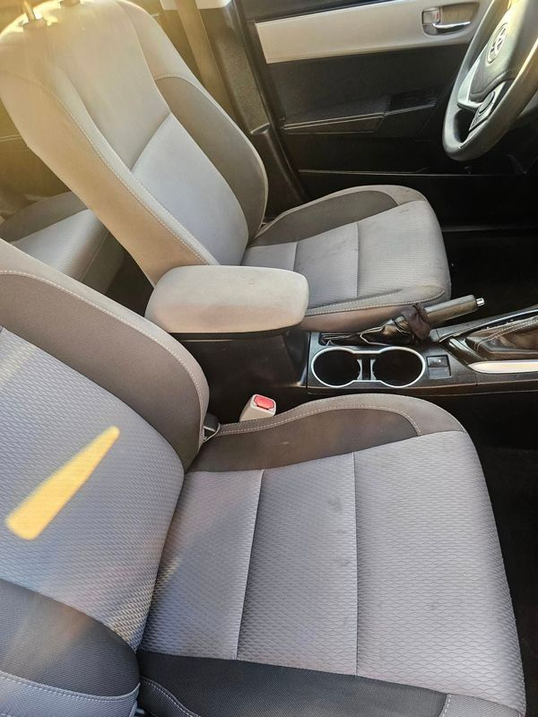Front passenger and driver seats in a car interior with grey fabric upholstery and a center console with cup holders.