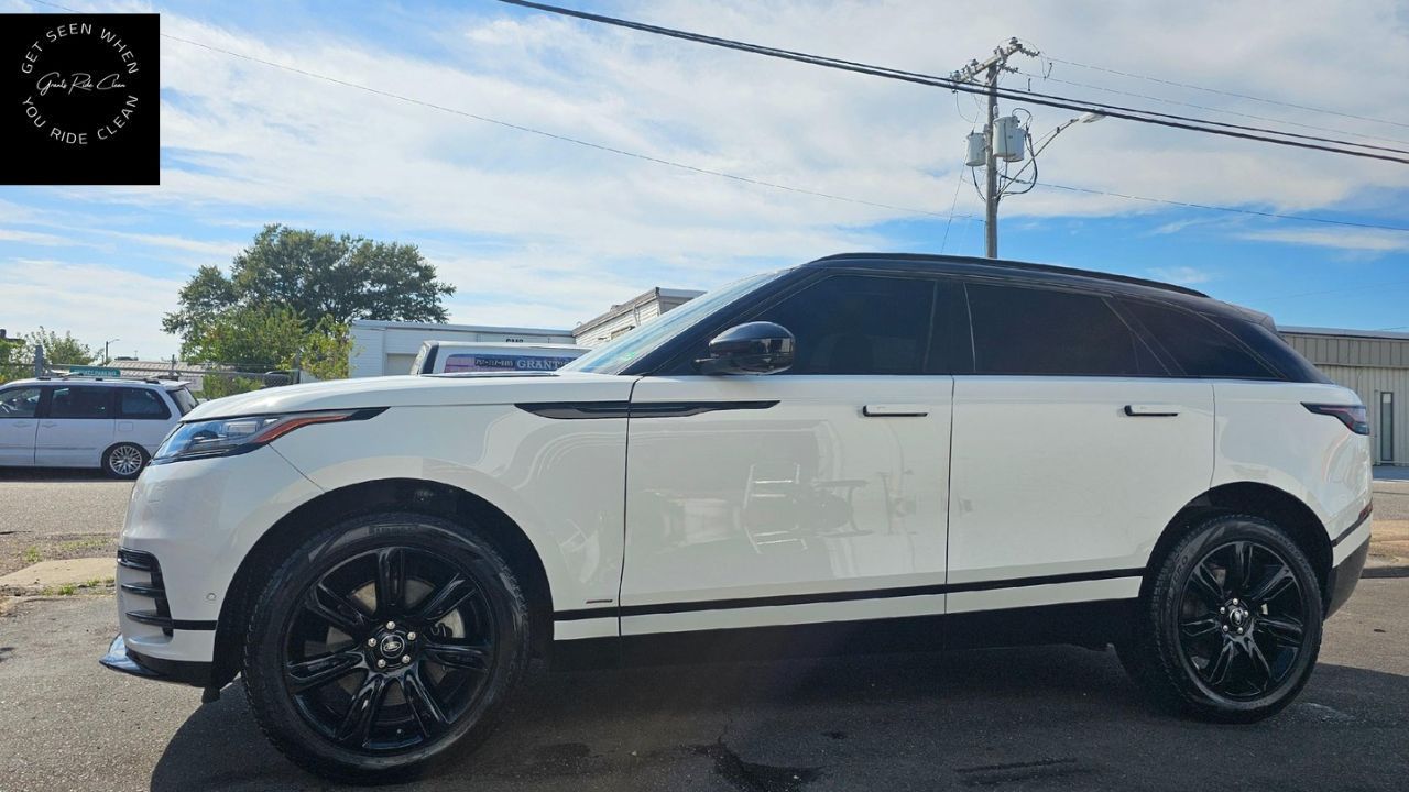 A white Land Rover Range Rover Velar SUV with black wheels parked on an asphalt lot under a blue sky.