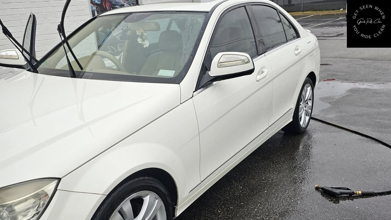 A white Mercedes-Benz sedan parked on a wet surface with its windshield wipers raised.