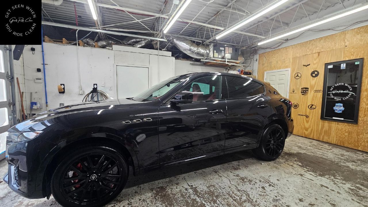 A black SUV parked inside a garage with bright overhead lighting and plywood walls.