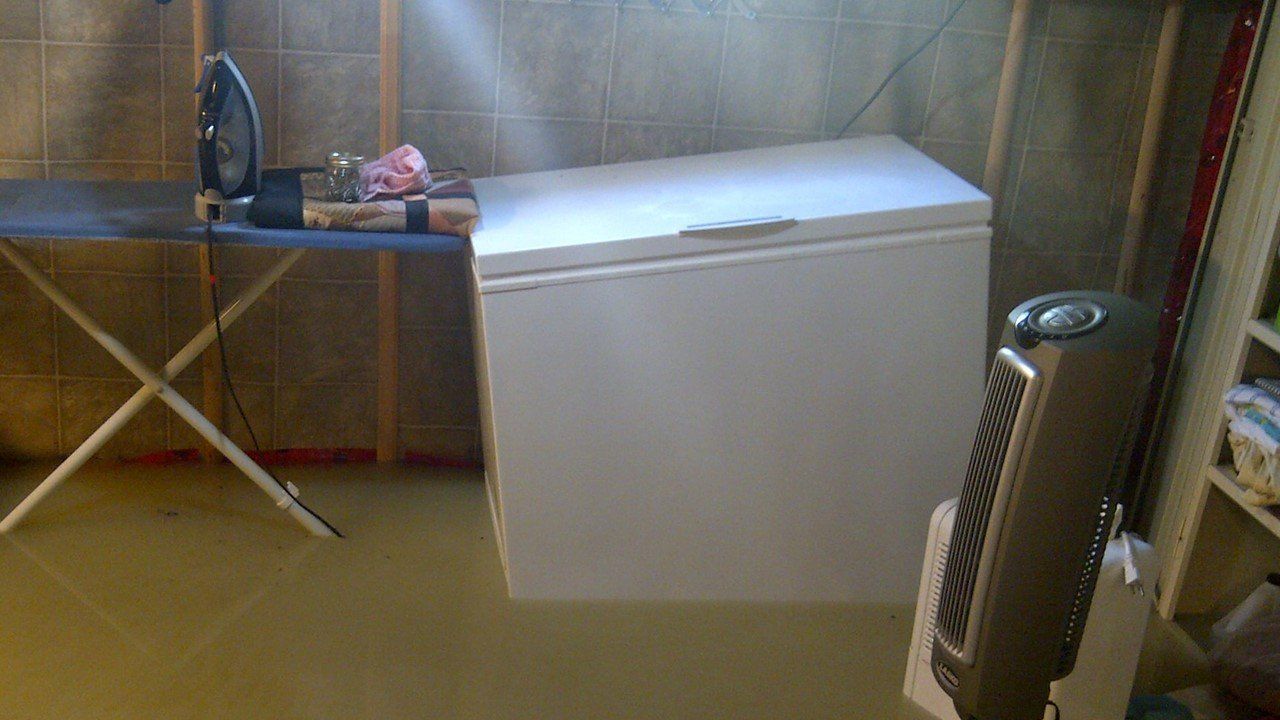 A flooded basement with a freezer and a fan.