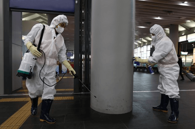 Two people in protective suits are spraying a building.