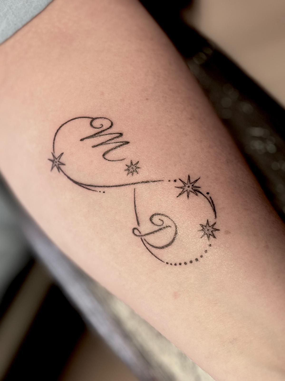Tattoo met een monogram in oneindigheidsstijl en sterren op de huid.