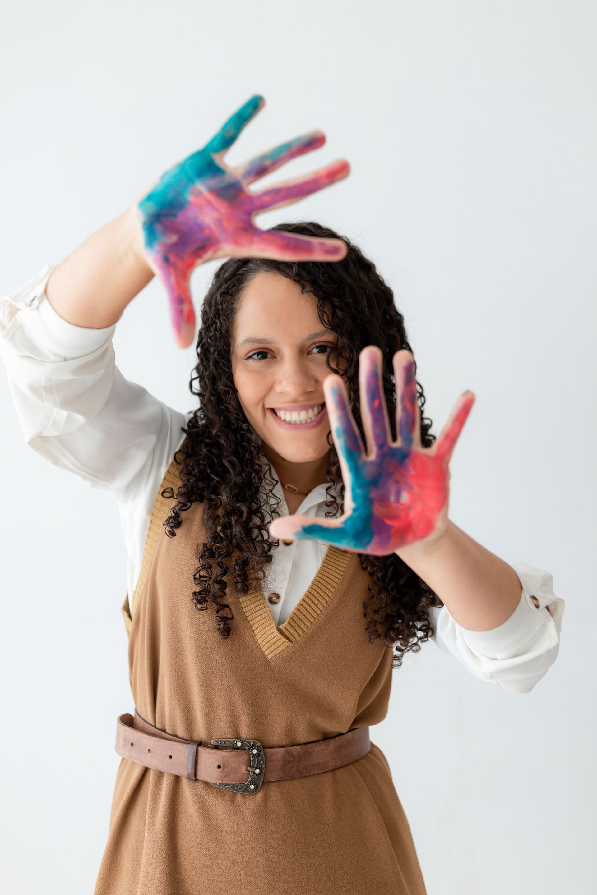 Uma mulher está fazendo uma moldura com as mãos pintadas em cores diferentes.