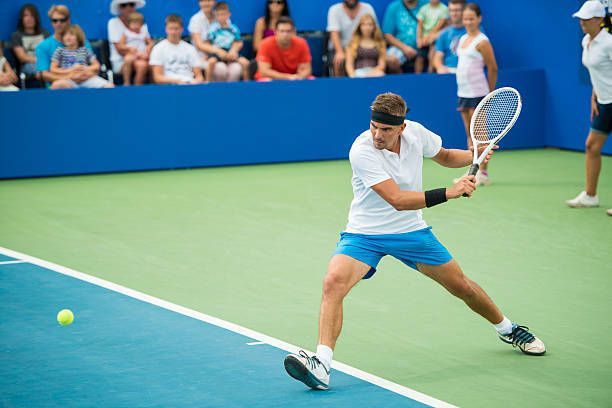 A man is teaching three children how to play tennis on a tennis court.