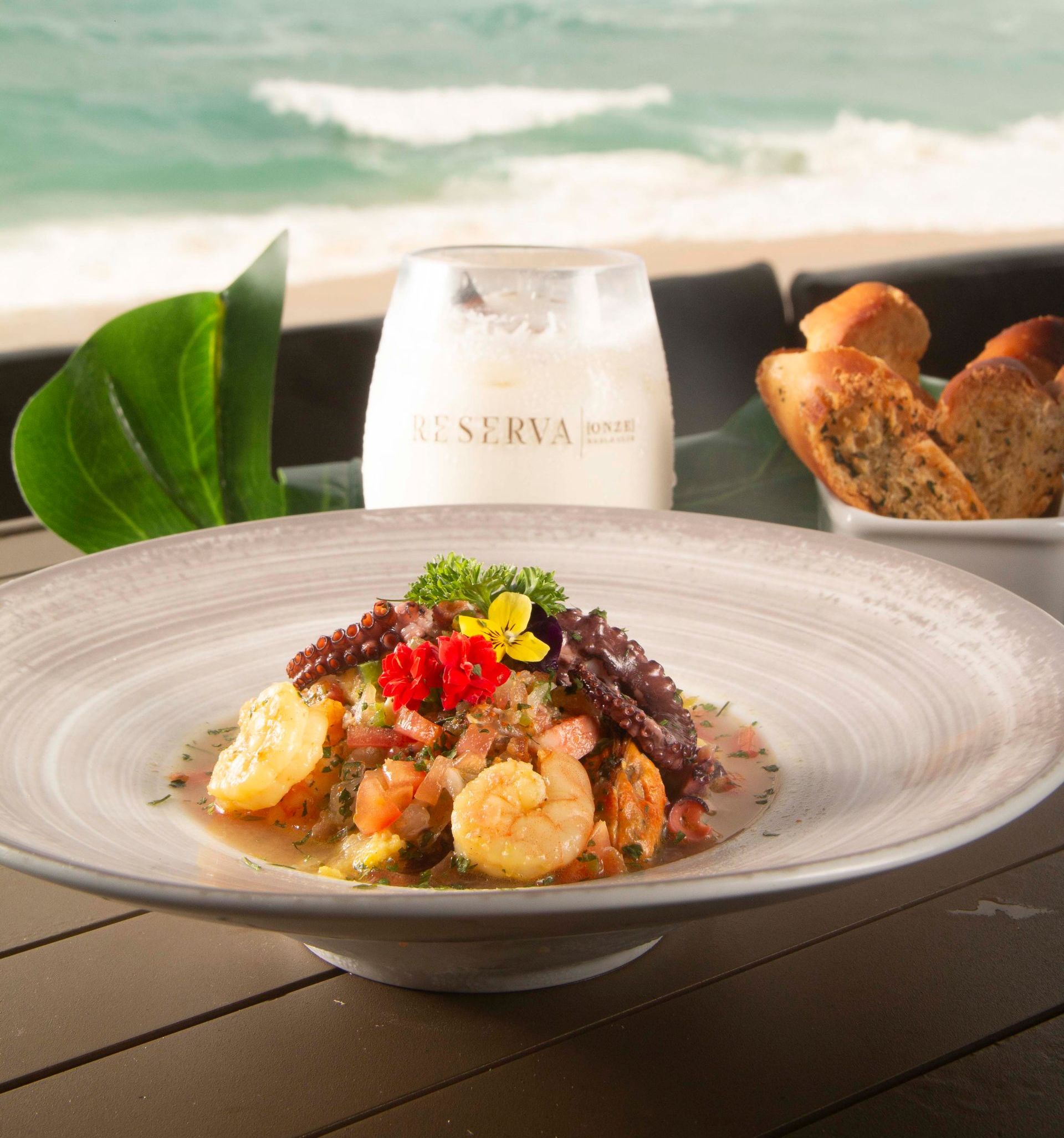 Prato de frutos do mar com camarão e polvo em um prato, com pão e bebida, fundo de praia.