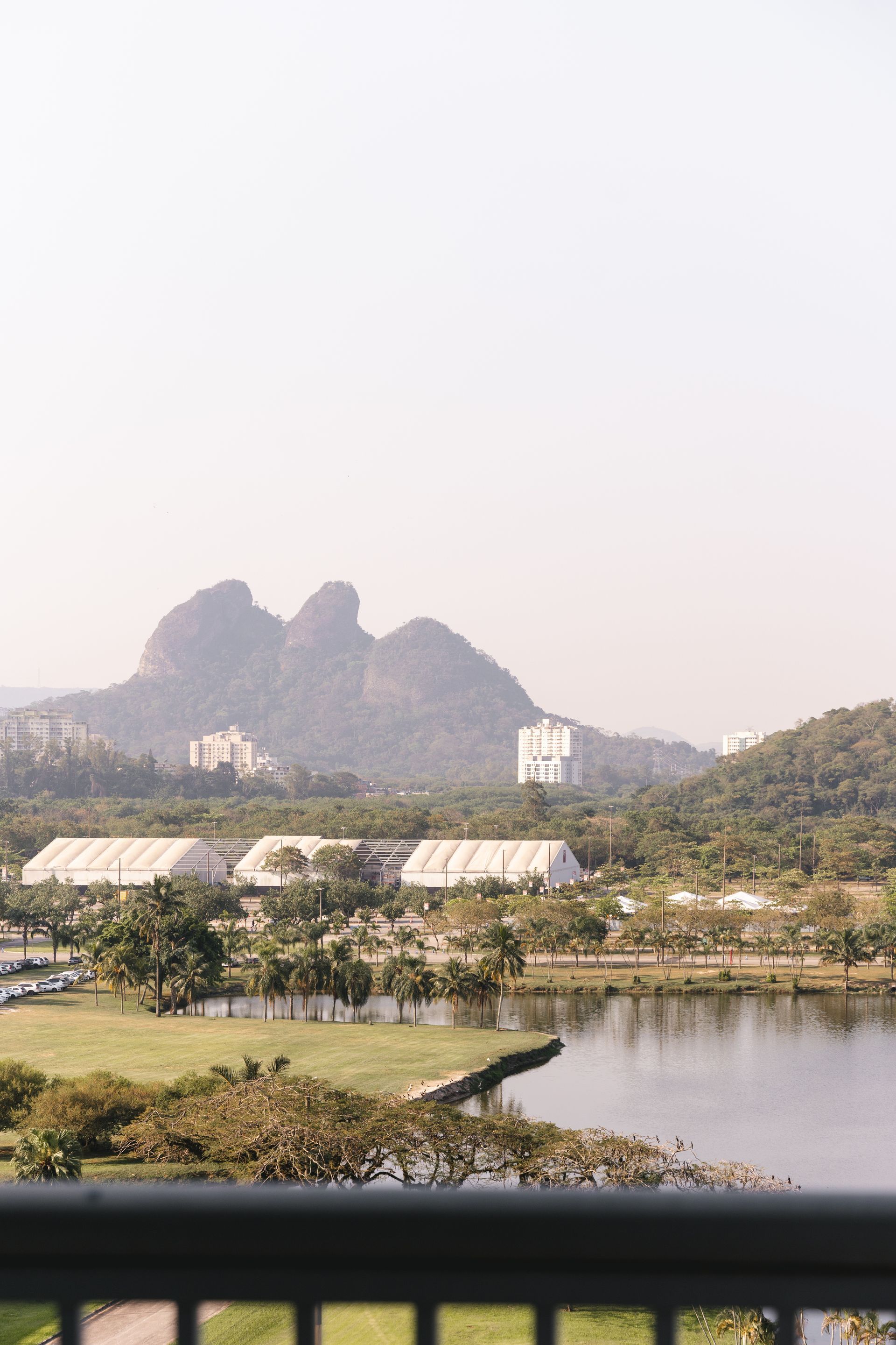 Com vista para um lago tranquilo, edifícios e árvores verdejantes se espalham para encontrar uma grande e acidentada montanha sob um céu nebuloso.