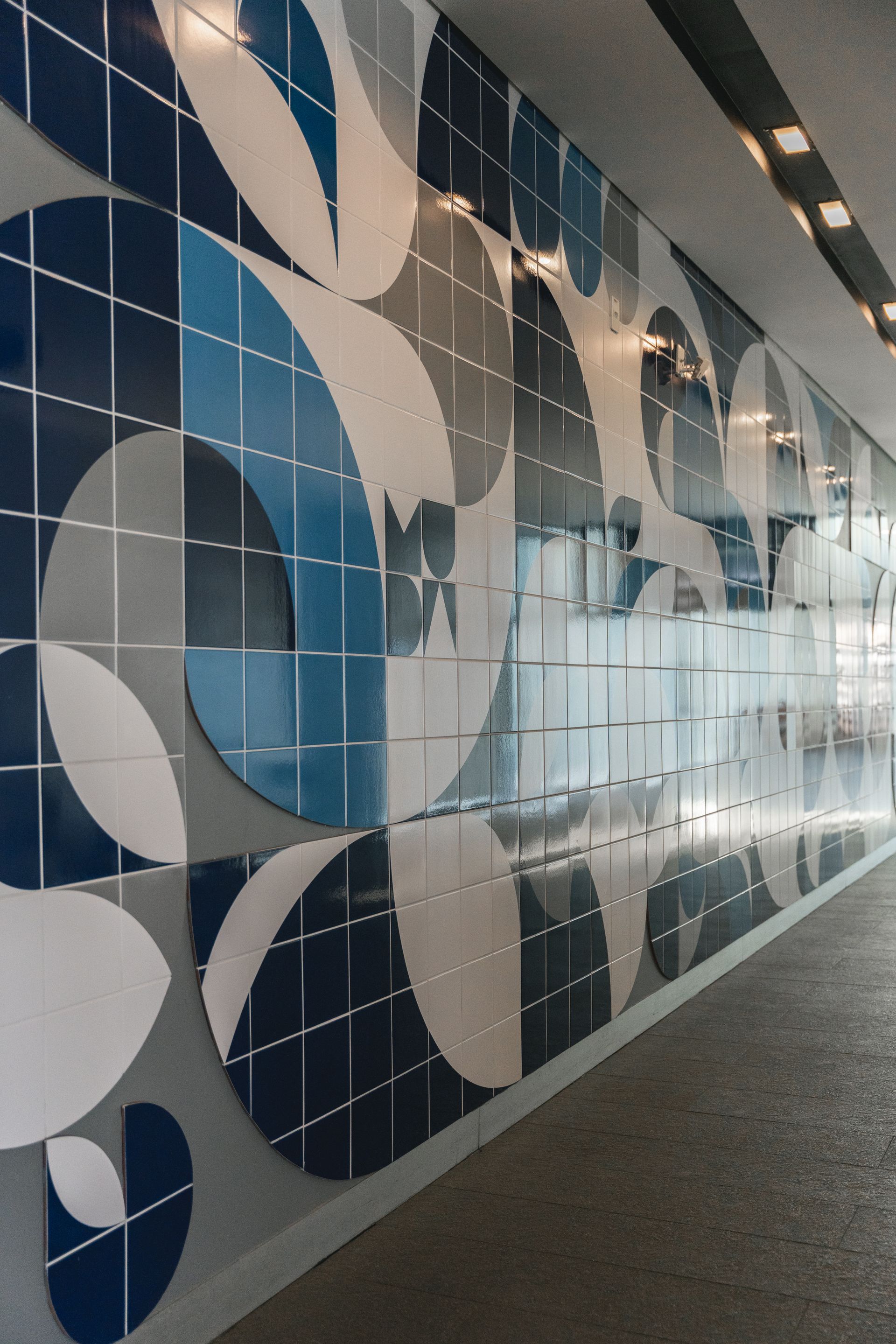 Mural de azulejos azuis e brancos em uma parede. Desenhos geométricos semicirculares em tons variados de azul, cinza e branco.