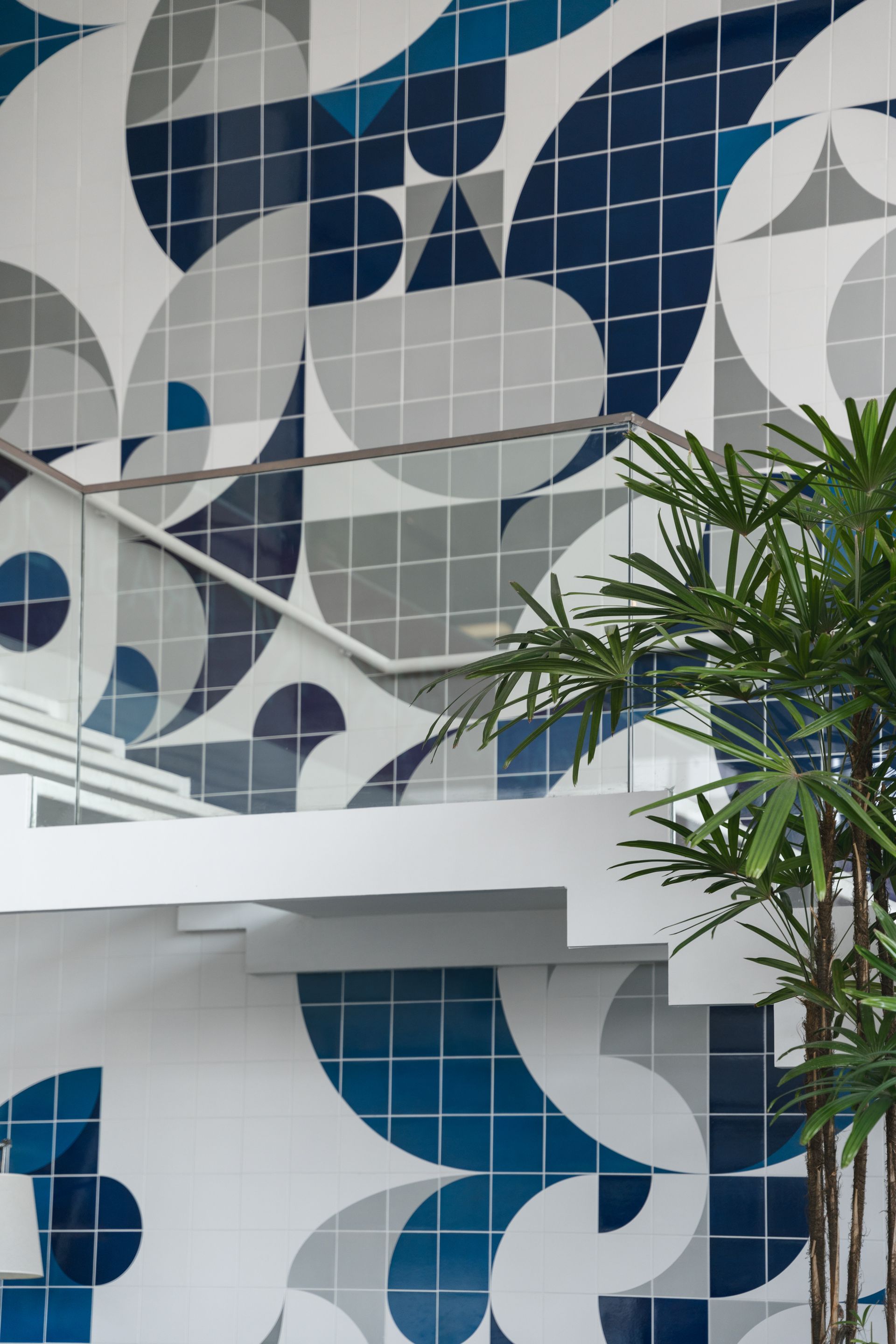 Escada branca com uma parede de azulejos geométricos modernos em azul, cinza e branco e uma planta verde à direita.