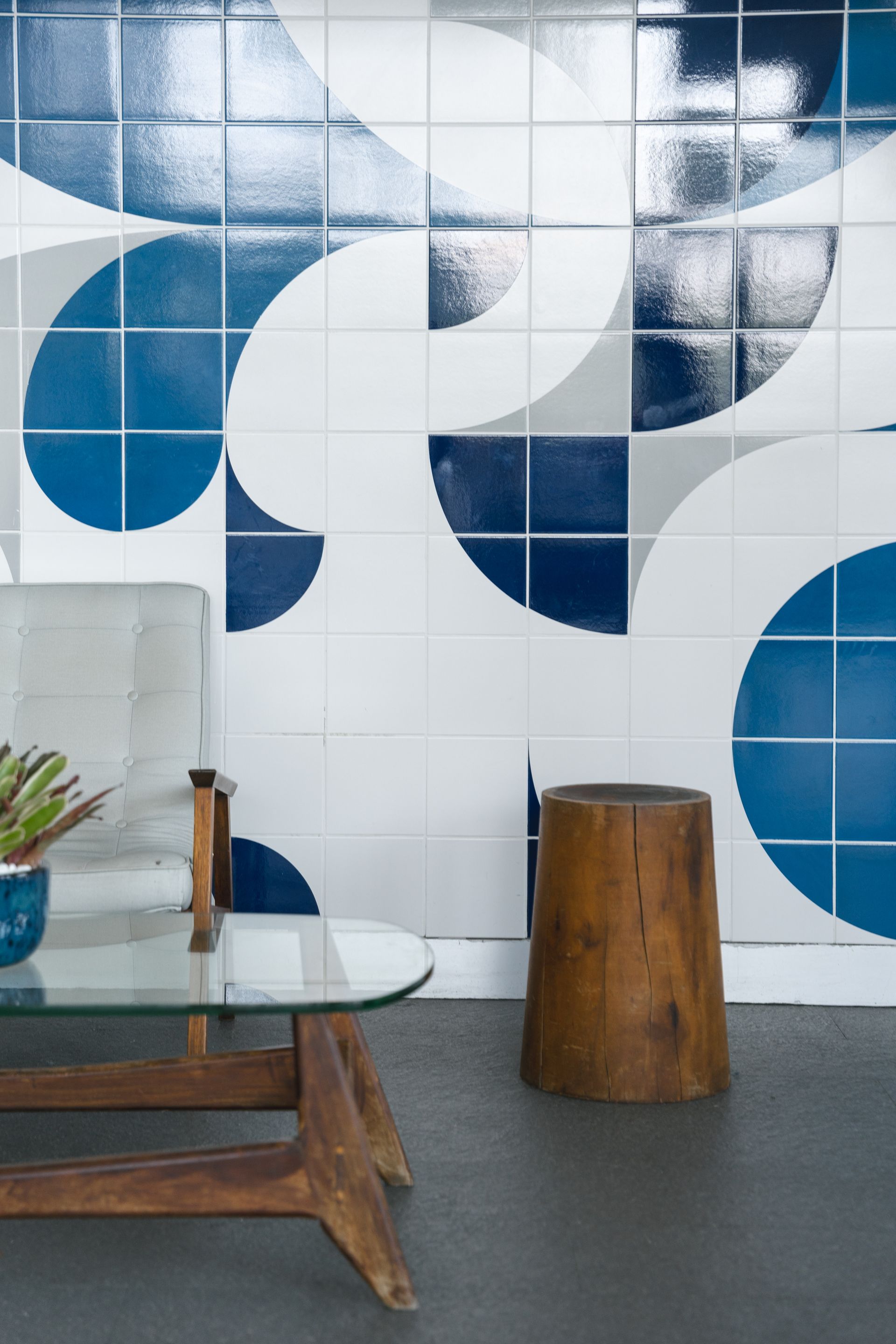 Parede de azulejos com padrões azuis e brancos, com uma cadeira moderna de meados do século e uma mesa lateral de madeira na frente.