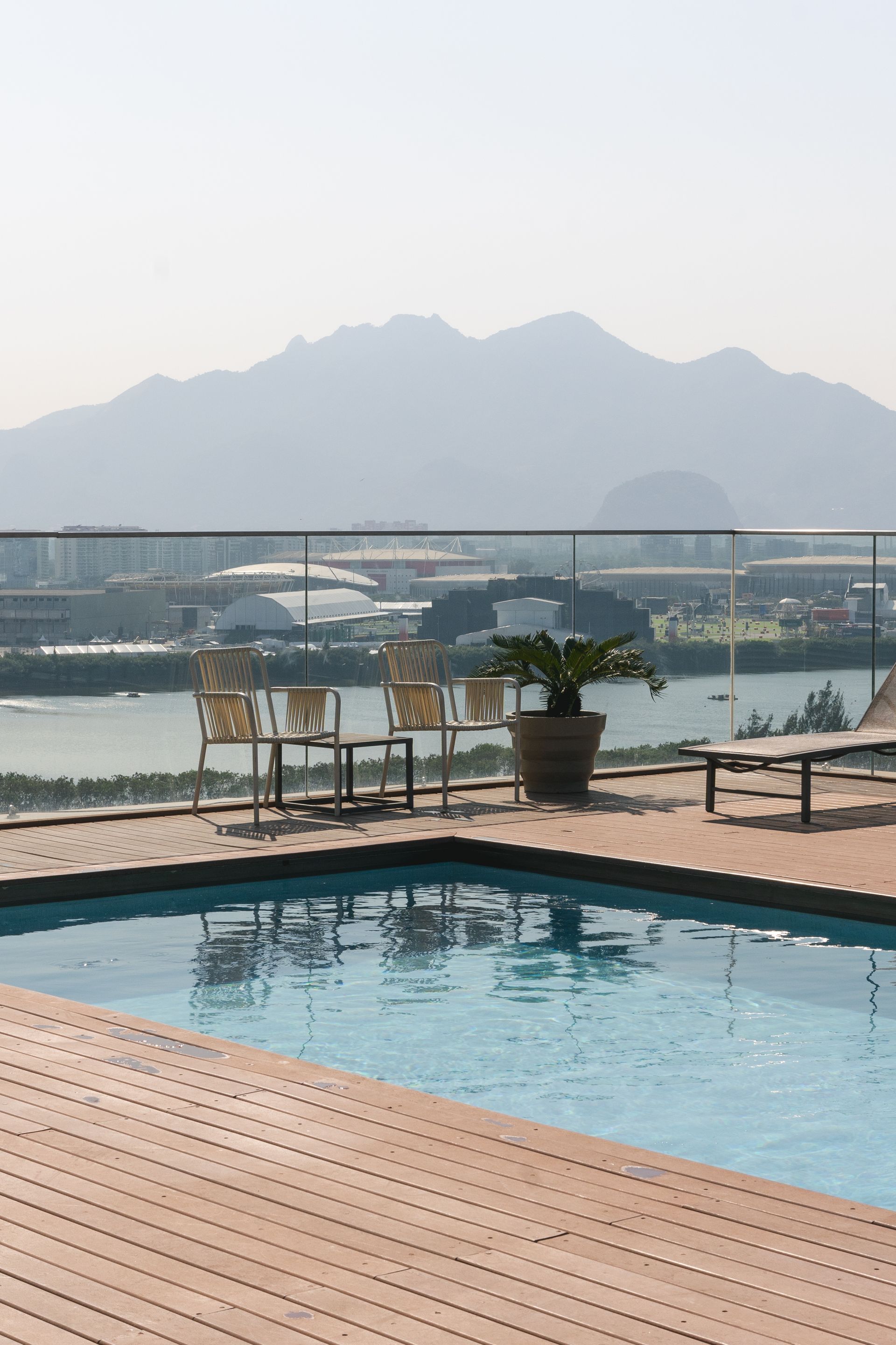 Piscina na cobertura com vista para as montanhas e um corpo d'água; cadeiras e vasos de plantas estão no deck.