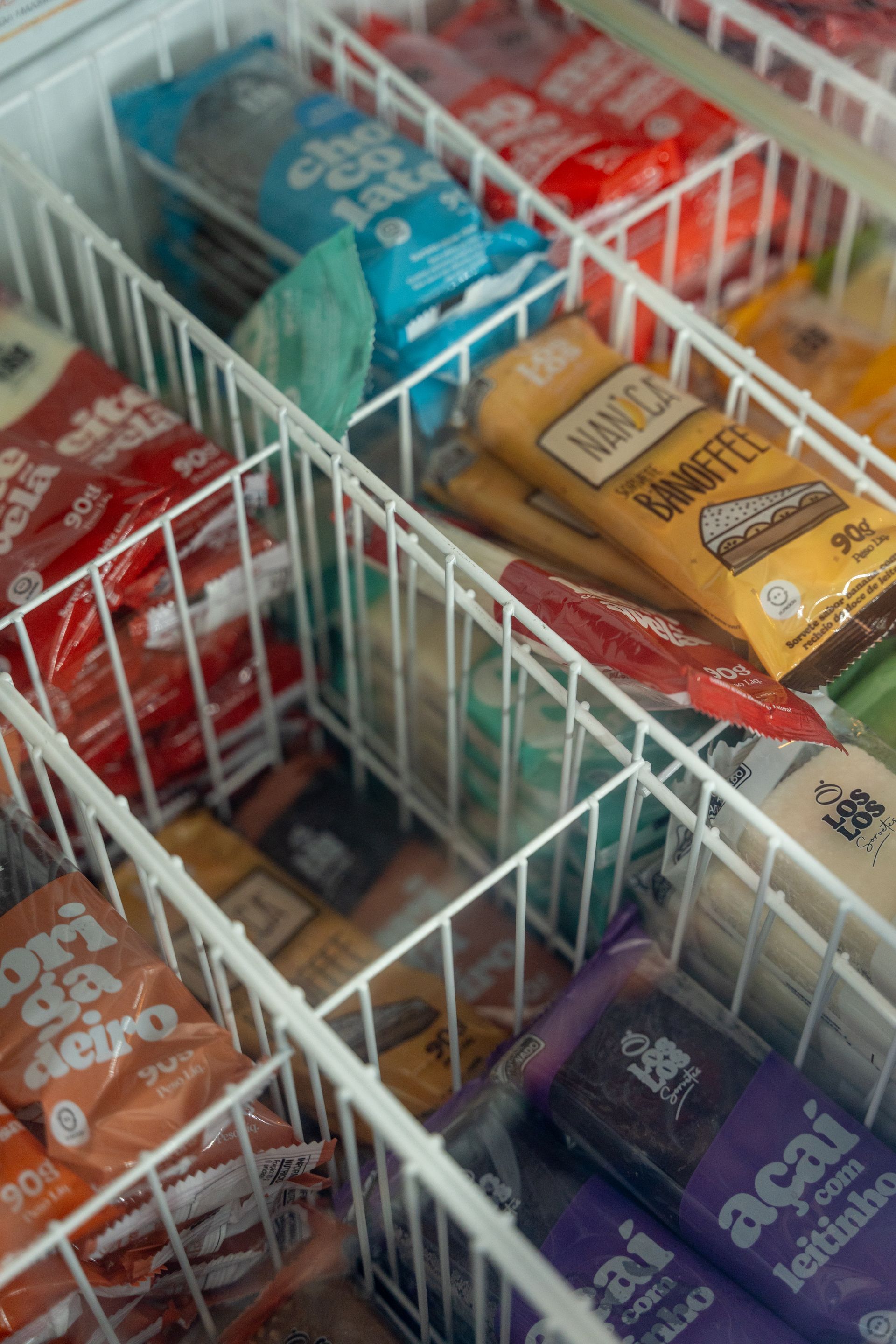 Congelador cheio de diversas barras de sorvete embaladas em cores diferentes, incluindo azul, vermelho, amarelo e roxo.