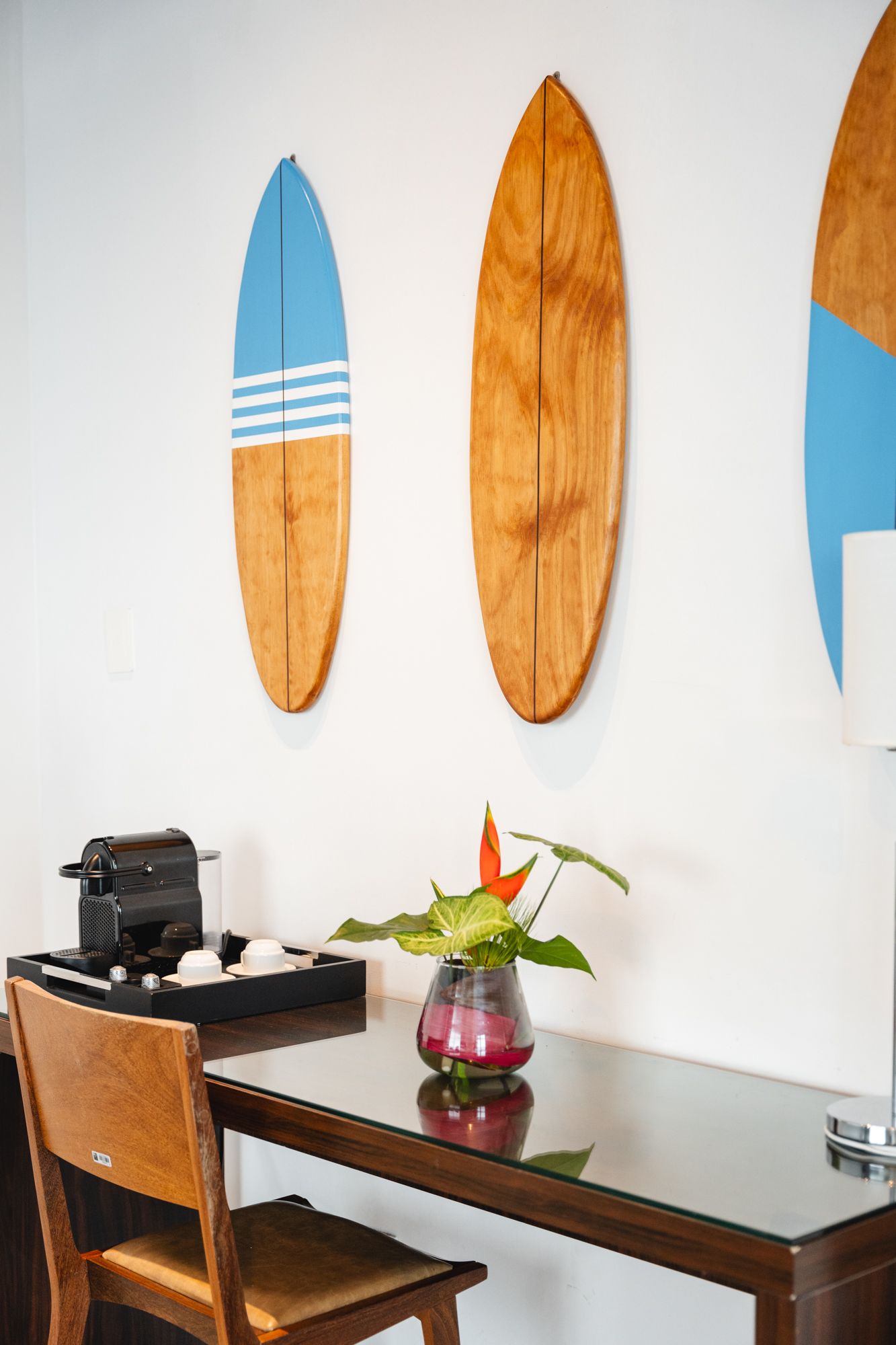 Uma mesa com uma cafeteira, uma cadeira e um vaso de flores, com pranchas de surfe penduradas na parede.