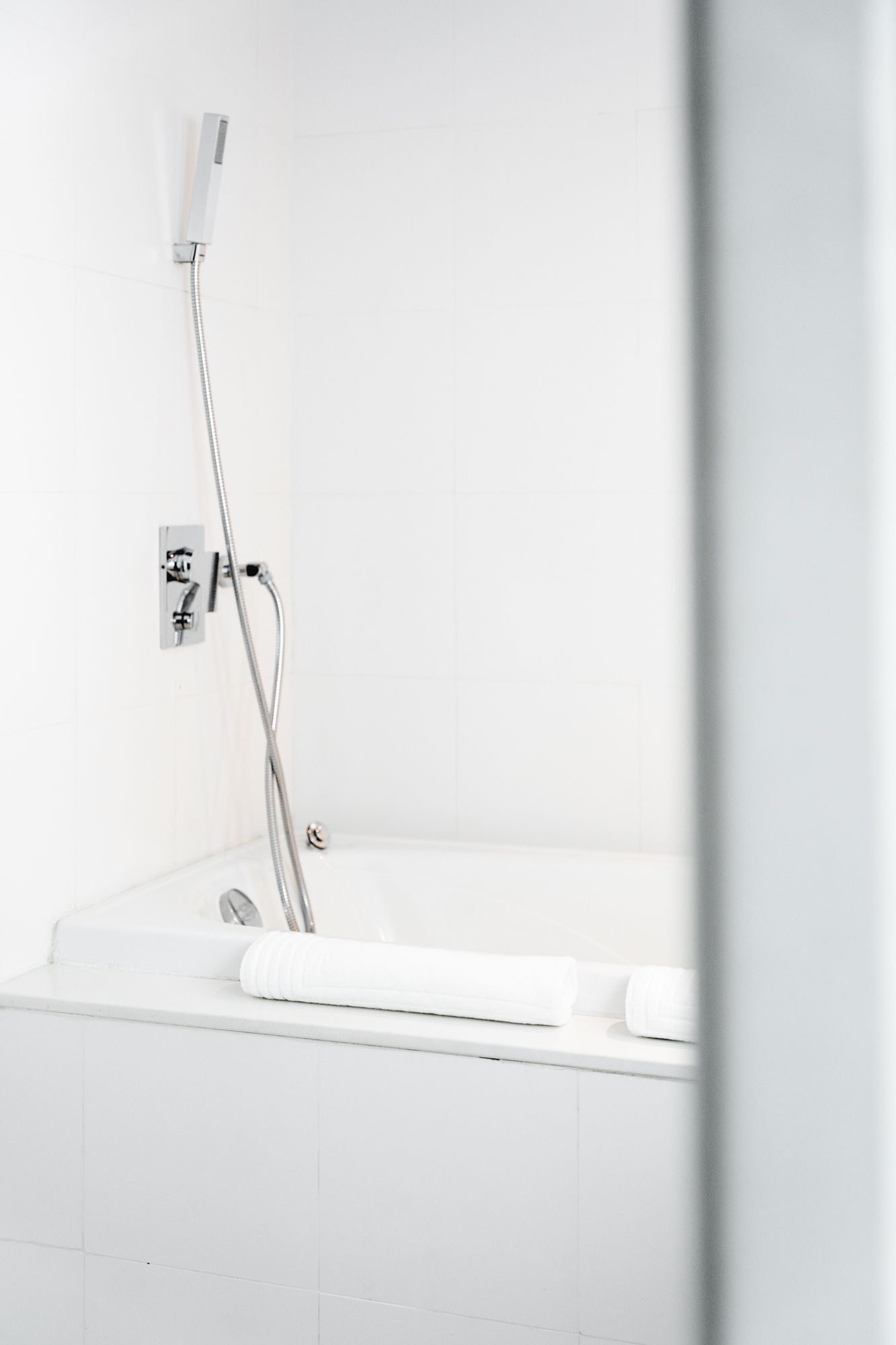 Banheira de hidromassagem branca com chuveiro e controles em uma parede branca.