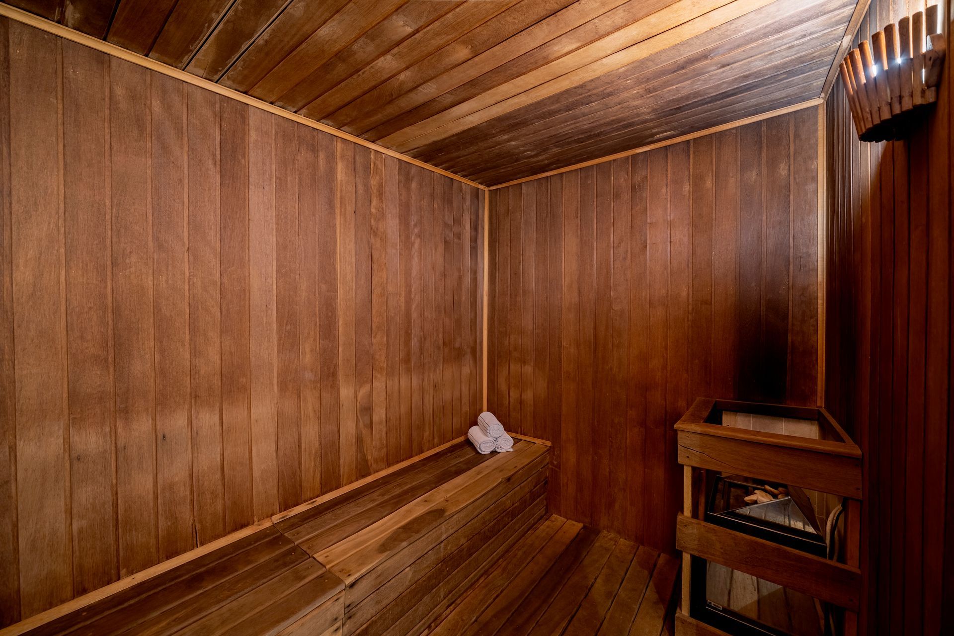 Uma sauna de madeira com bancos, paredes e teto. Duas toalhas brancas repousam sobre um banco.