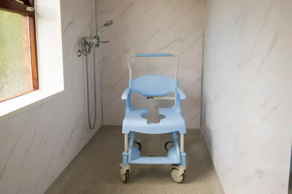 Oaklands Residential Care Home, Methley, Leeds | A blue wheelchair is sitting in a bathroom next to a window.