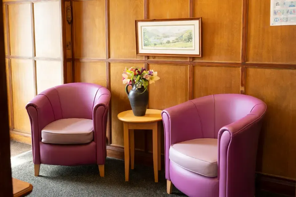 Oaklands Residential Care Home, Methley, Leeds | Two purple chairs are sitting next to a table with a vase of flowers on it.