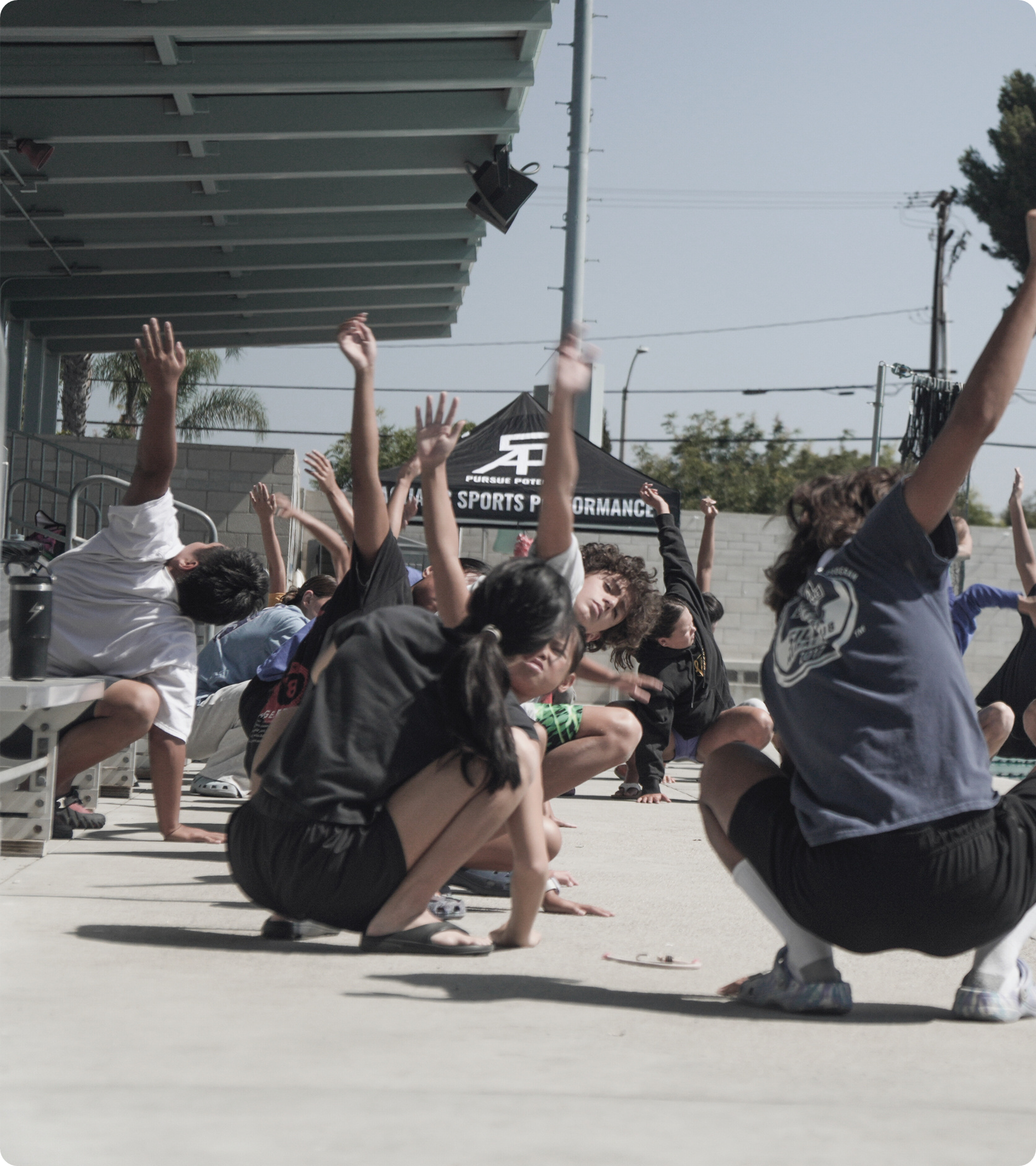 Group of people doing exercise outdoors with arms raised.